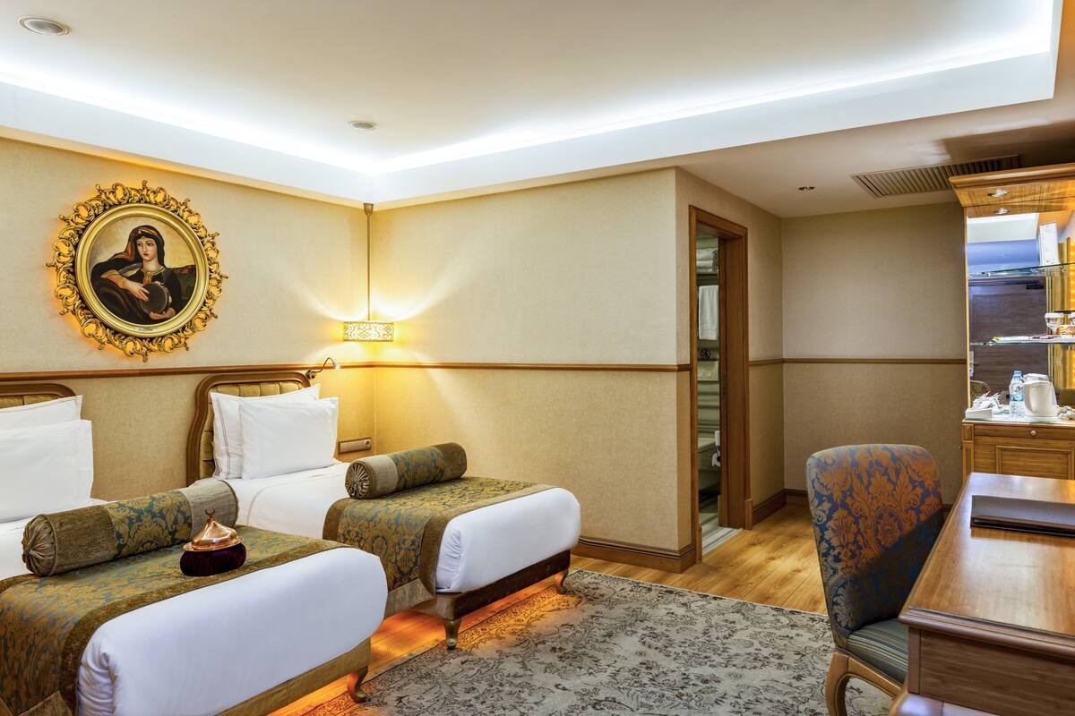 A hotel room with two beds, a desk, a chair, a lamp, and a painting on the wall.