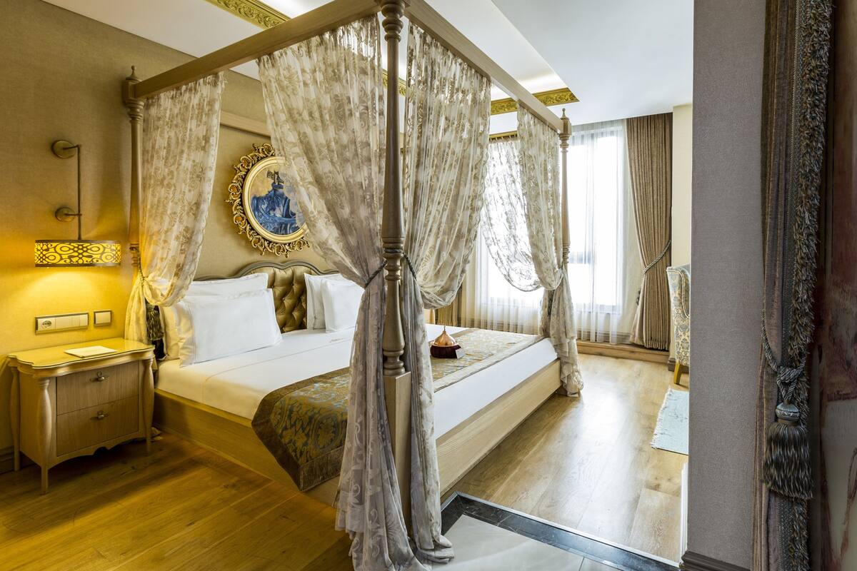 A four-poster canopy bed with a gold frame, a bedside table with a lamp, and a large mirror on the wall.