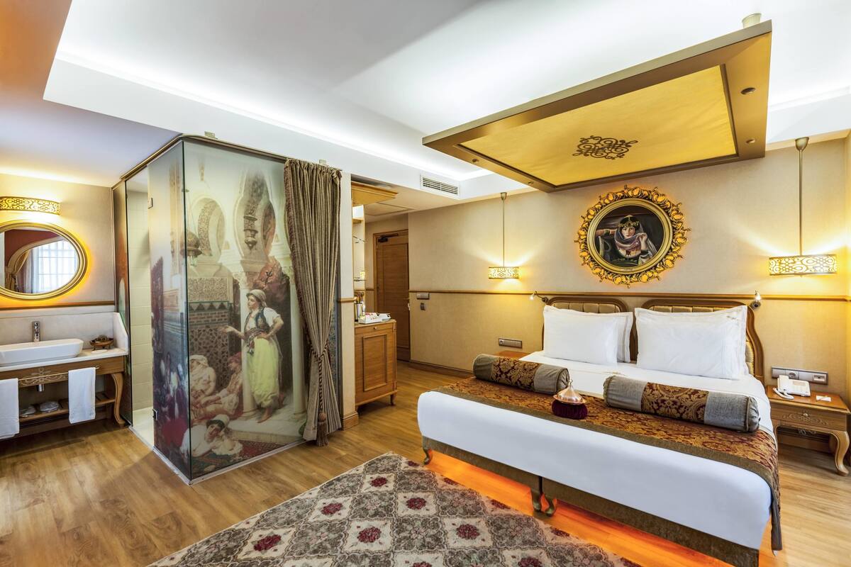 A hotel room with a large bed, a bathroom with a sink and mirror, and a decorative wall with a framed picture.