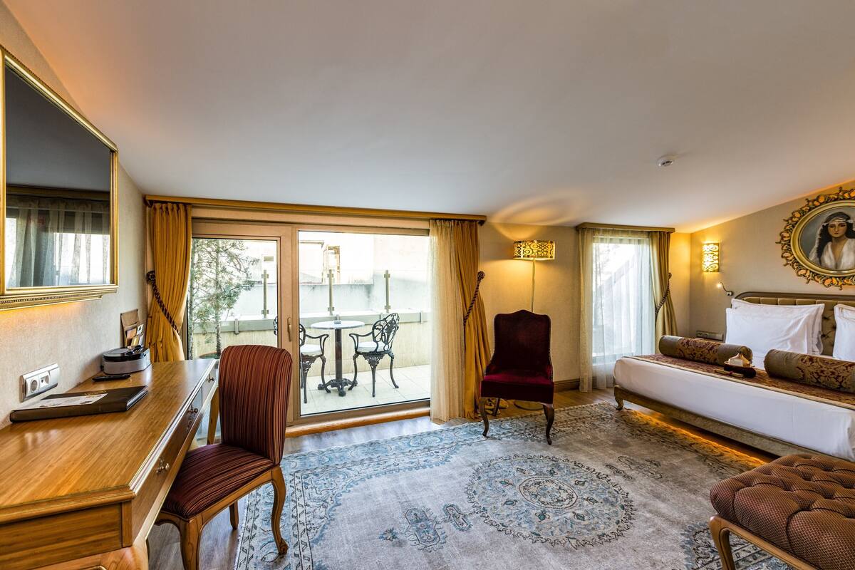 A hotel room with a bed, a desk, a chair, a sofa, a rug, and a view of the outdoors.
