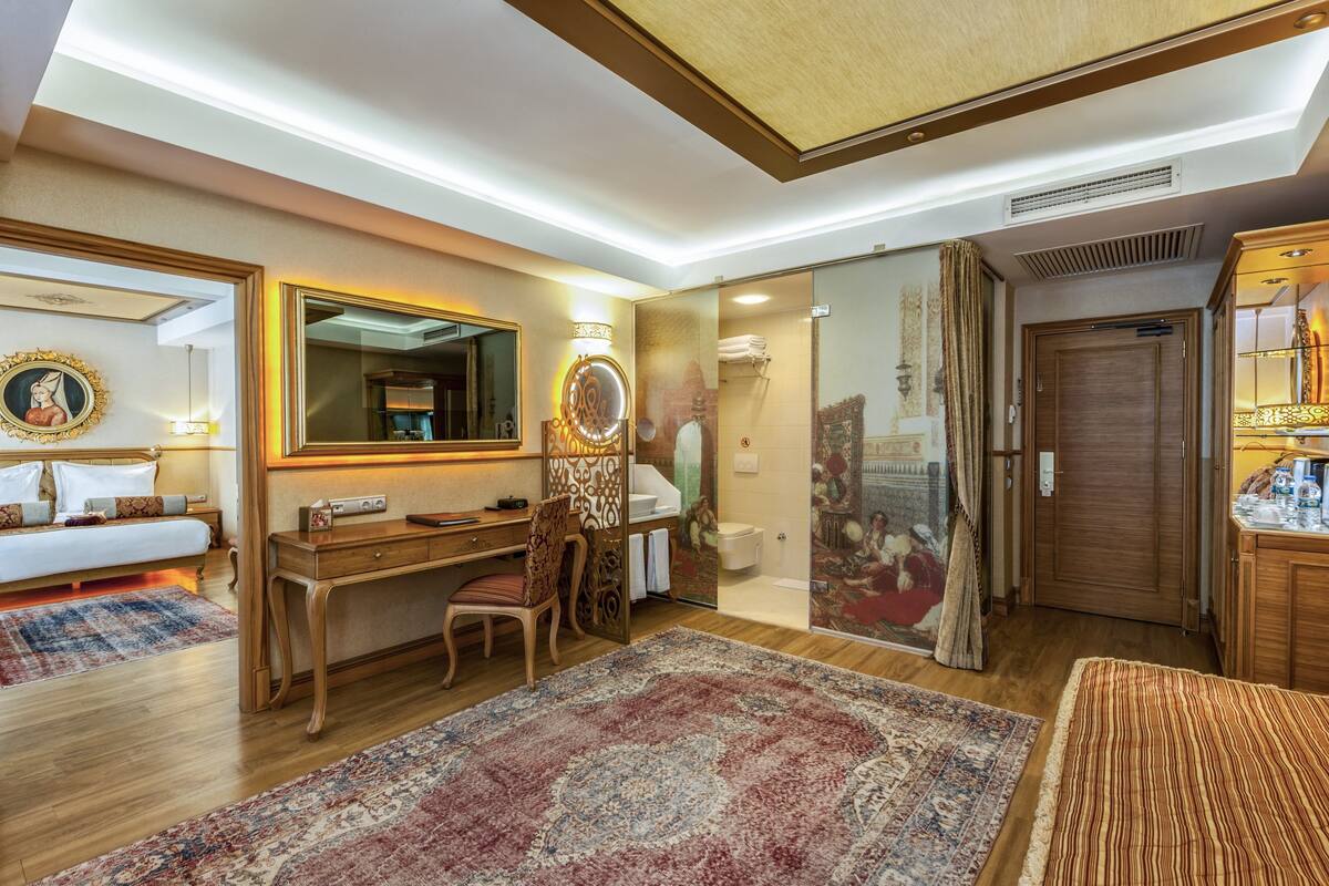 A hotel room with a bed, desk, chair, and a large mirror.