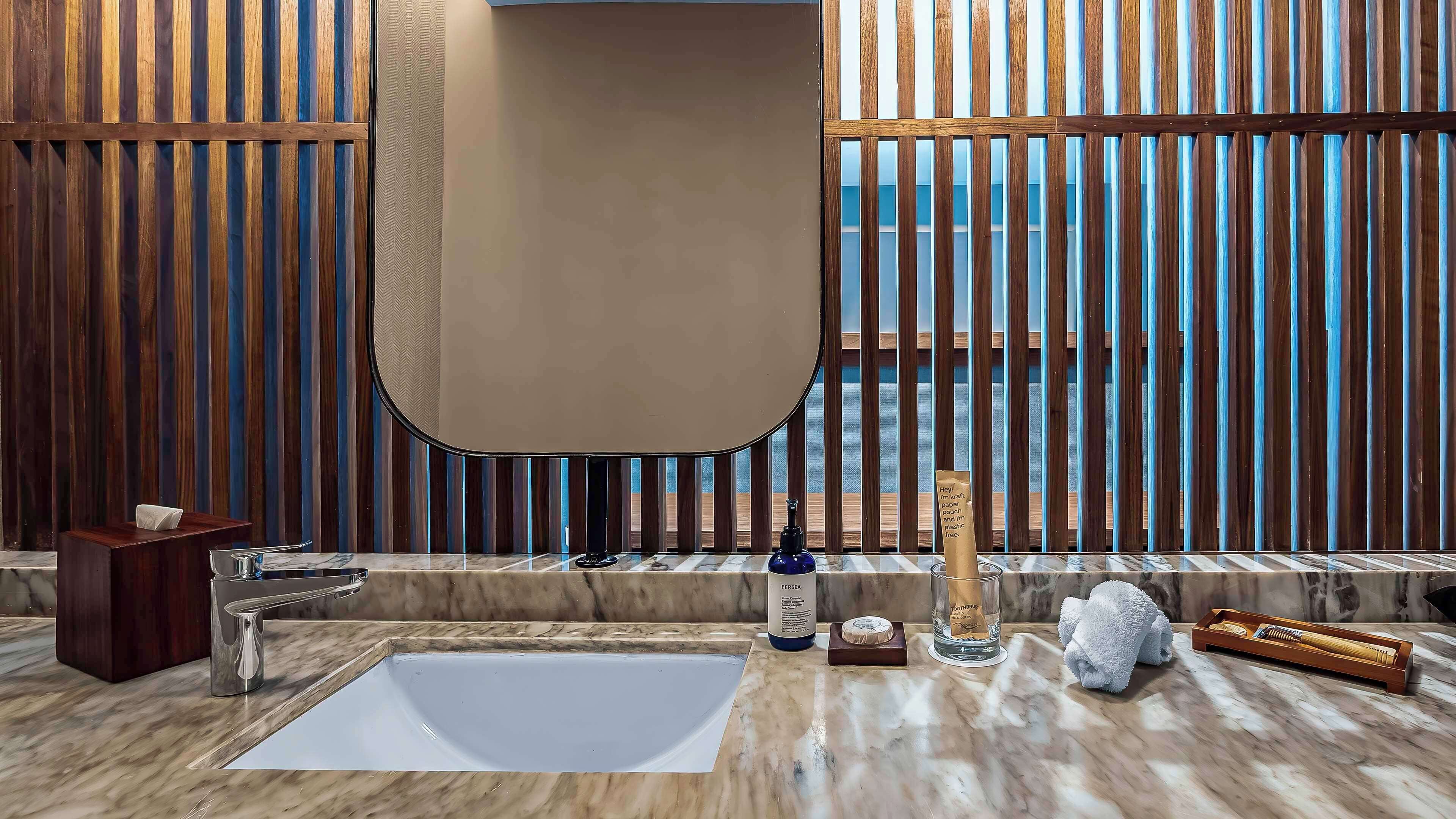 Un baño moderno con un espejo grande, encimera de mármol y paneles de madera.
