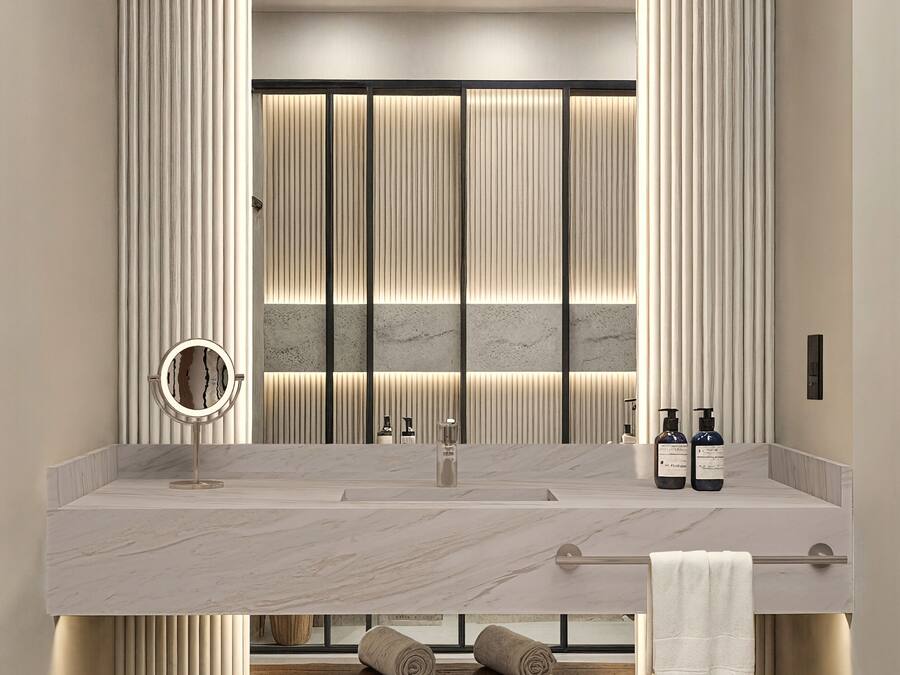 A modern bathroom with a large marble sink, a round mirror, and a bench with towels.