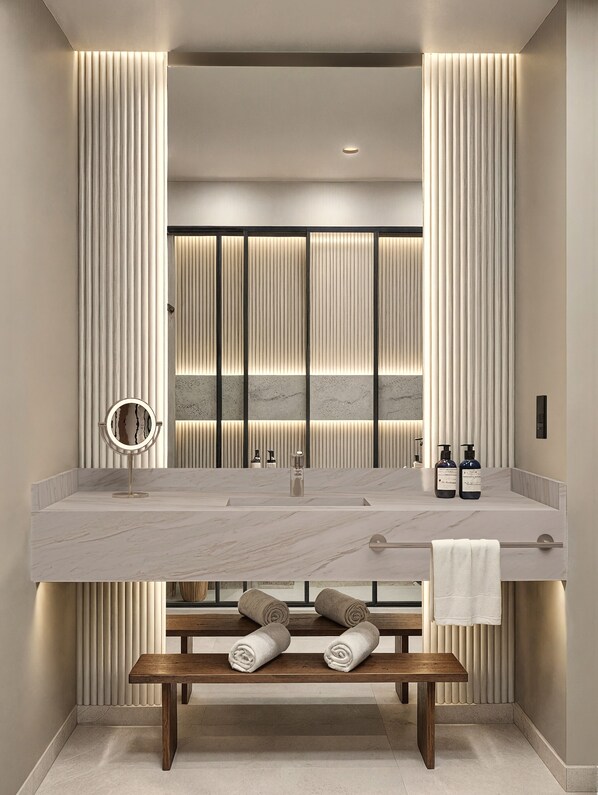 Un baño moderno con un lavamanos grande de mármol, un espejo redondo y un banco con toallas.