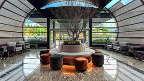 A modern lobby with a central seating area, a large tree, and a view of the outdoors. - Hilton Queretaro (Querétaro)