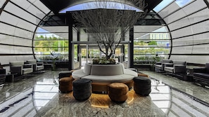A modern lobby with a central seating area, a large tree, and a view of the outdoors. - Hilton Queretaro (Querétaro)