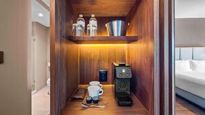 Habitación compacta y bien iluminada con detalles de madera, una cafetera, dos tazas, una cuchara y una pequeña bandeja con aderezos.