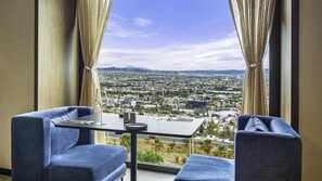 Una habitación con una mesa y dos sillas, vista panorámica de la ciudad a través de amplias ventanas y cortinas.