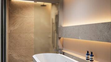 Un baño moderno con una bañera independiente, zona de ducha y tocador con botellas.