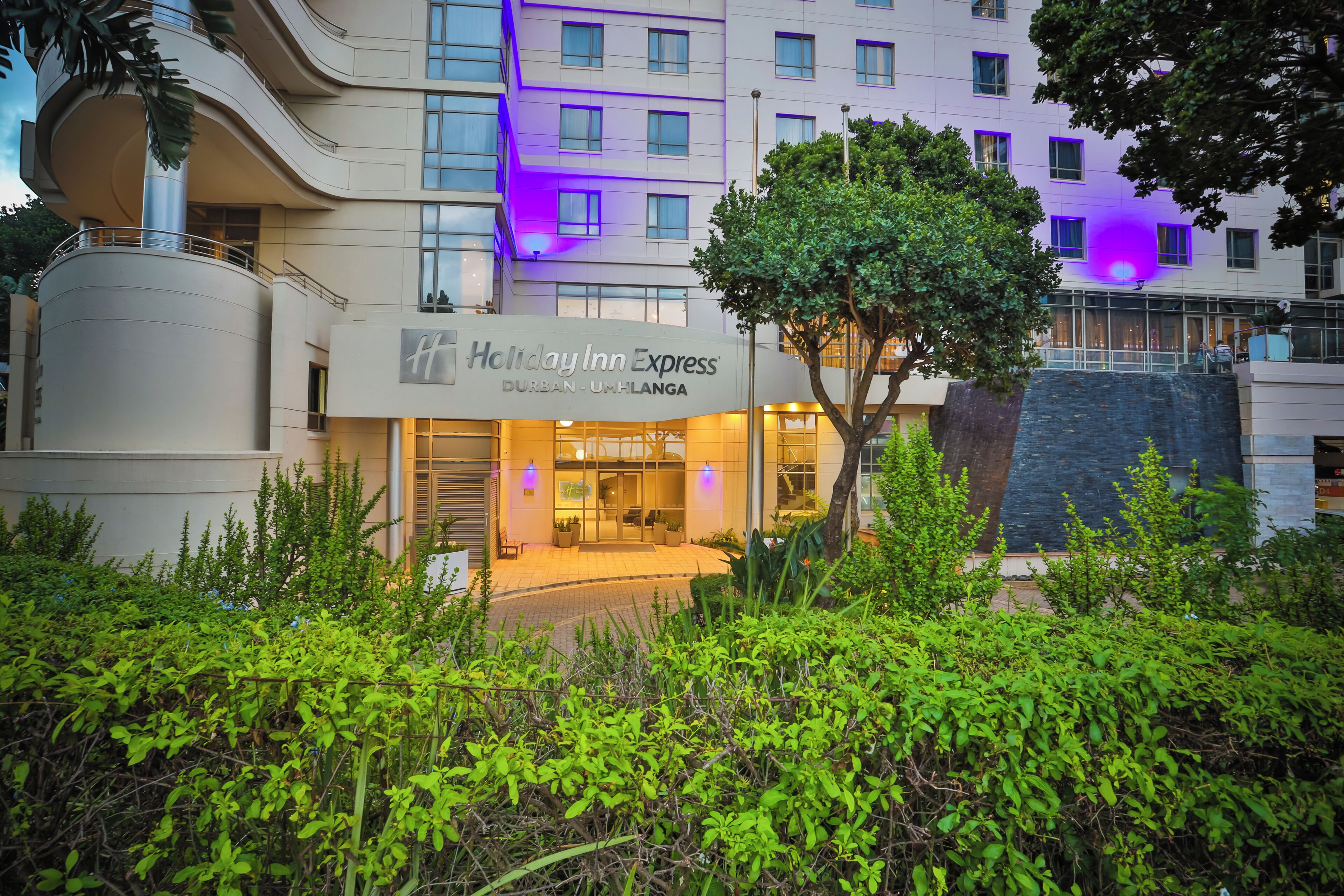 A Holiday Inn Express building with a modern design, featuring a prominent entrance and a tree in the foreground.