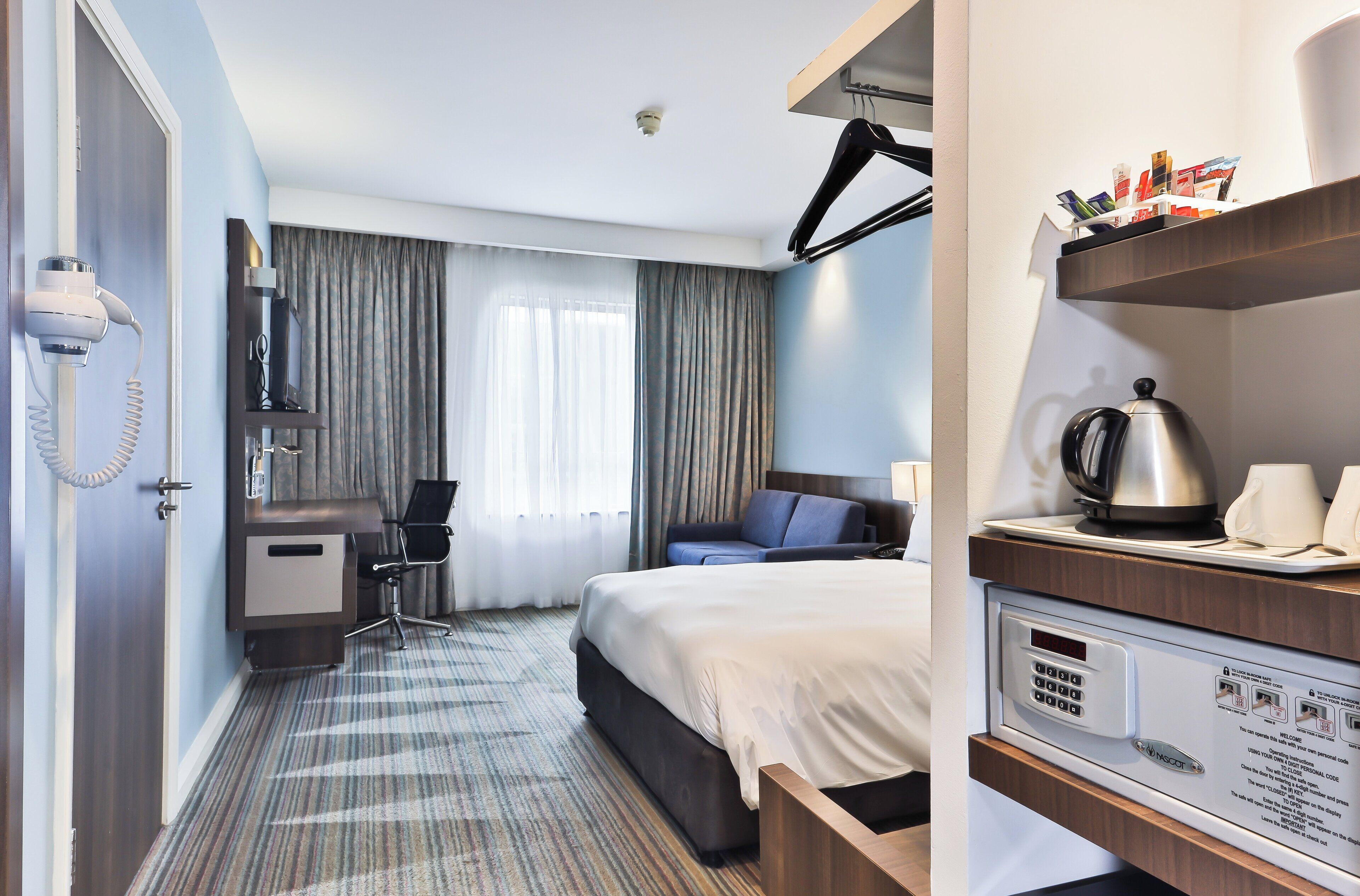 A hotel room with a bed, desk, chair, and a minibar.