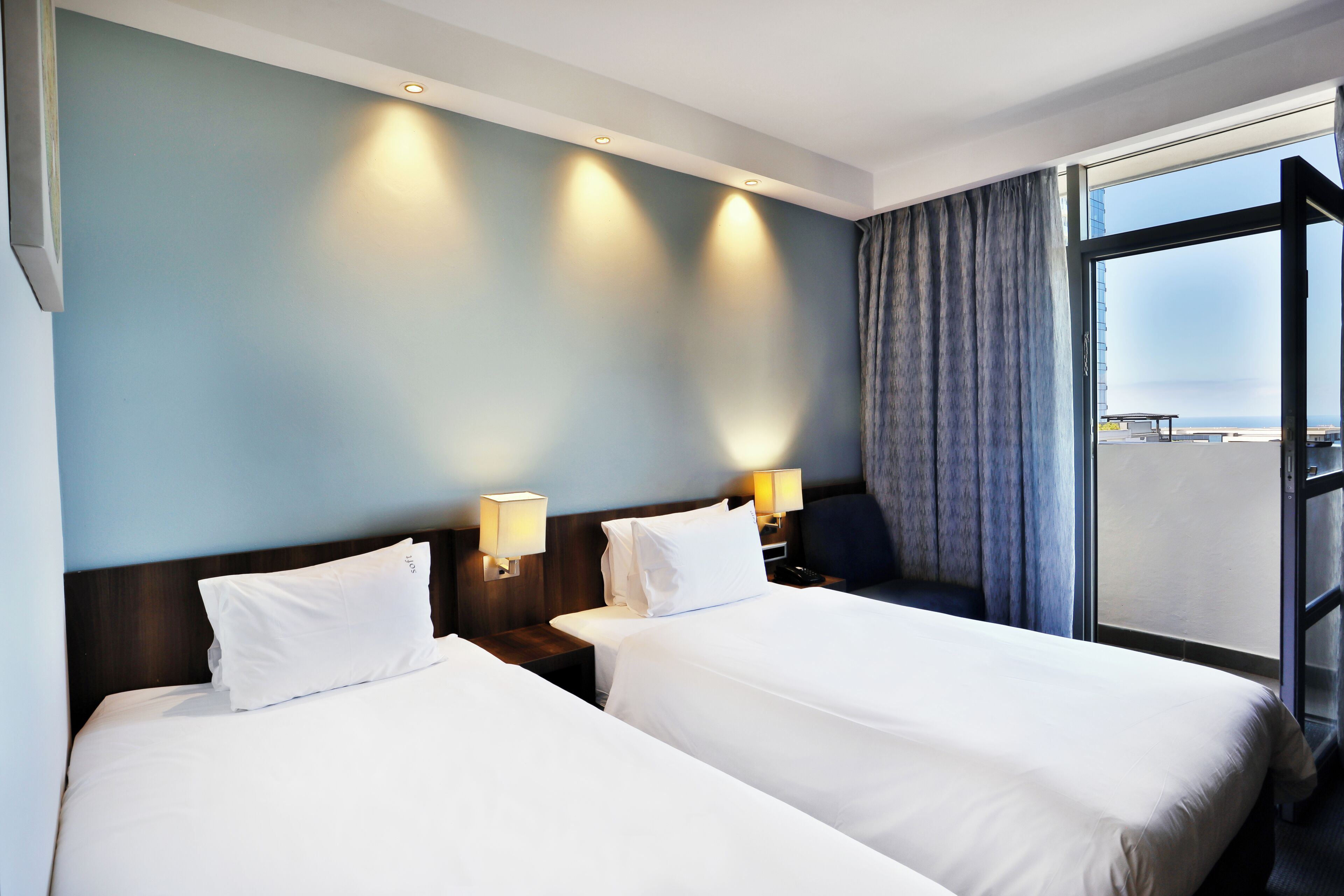 A hotel room with two beds, a large window, and a view of the city.