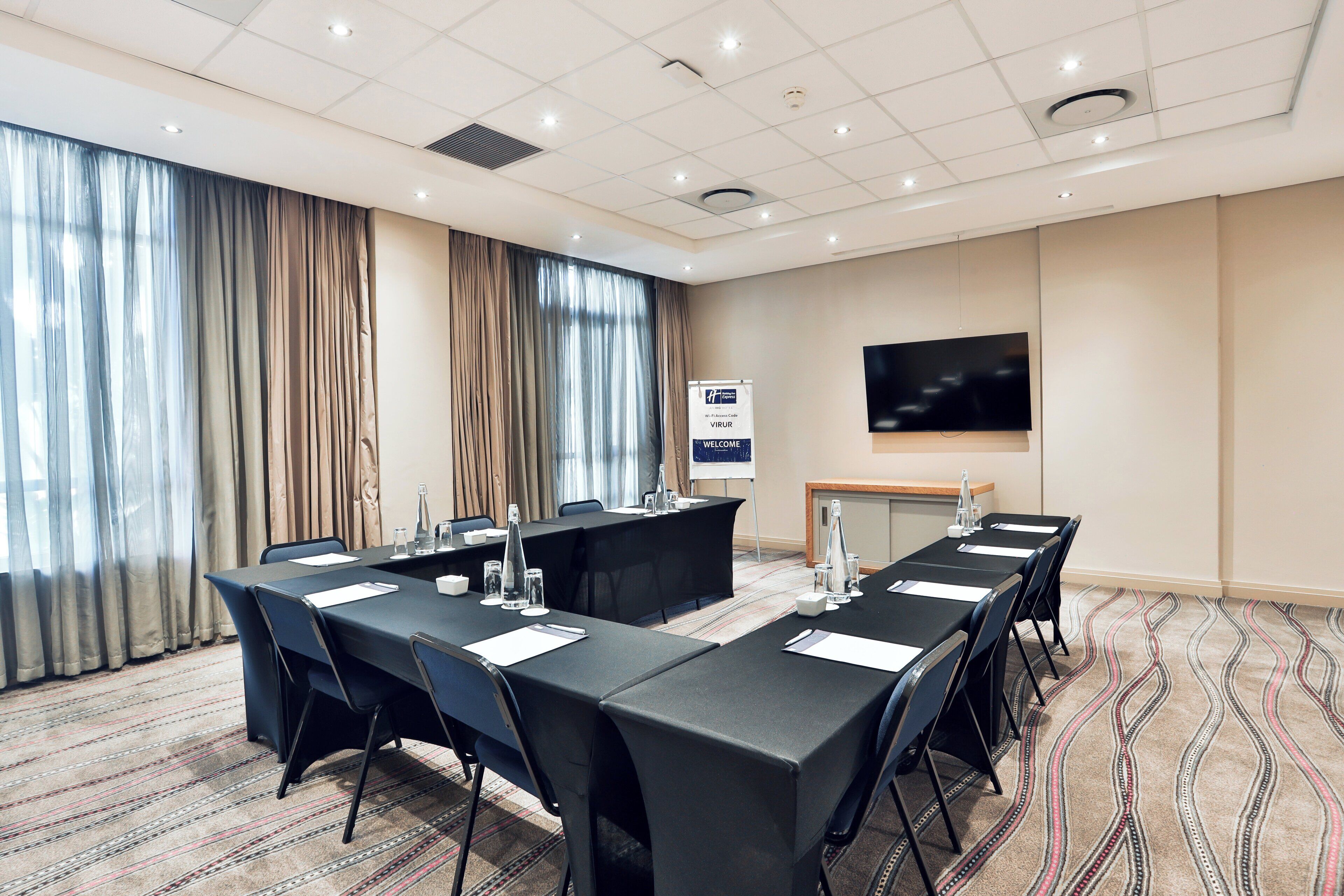A conference room with a long table, chairs, a projector screen, and a television.