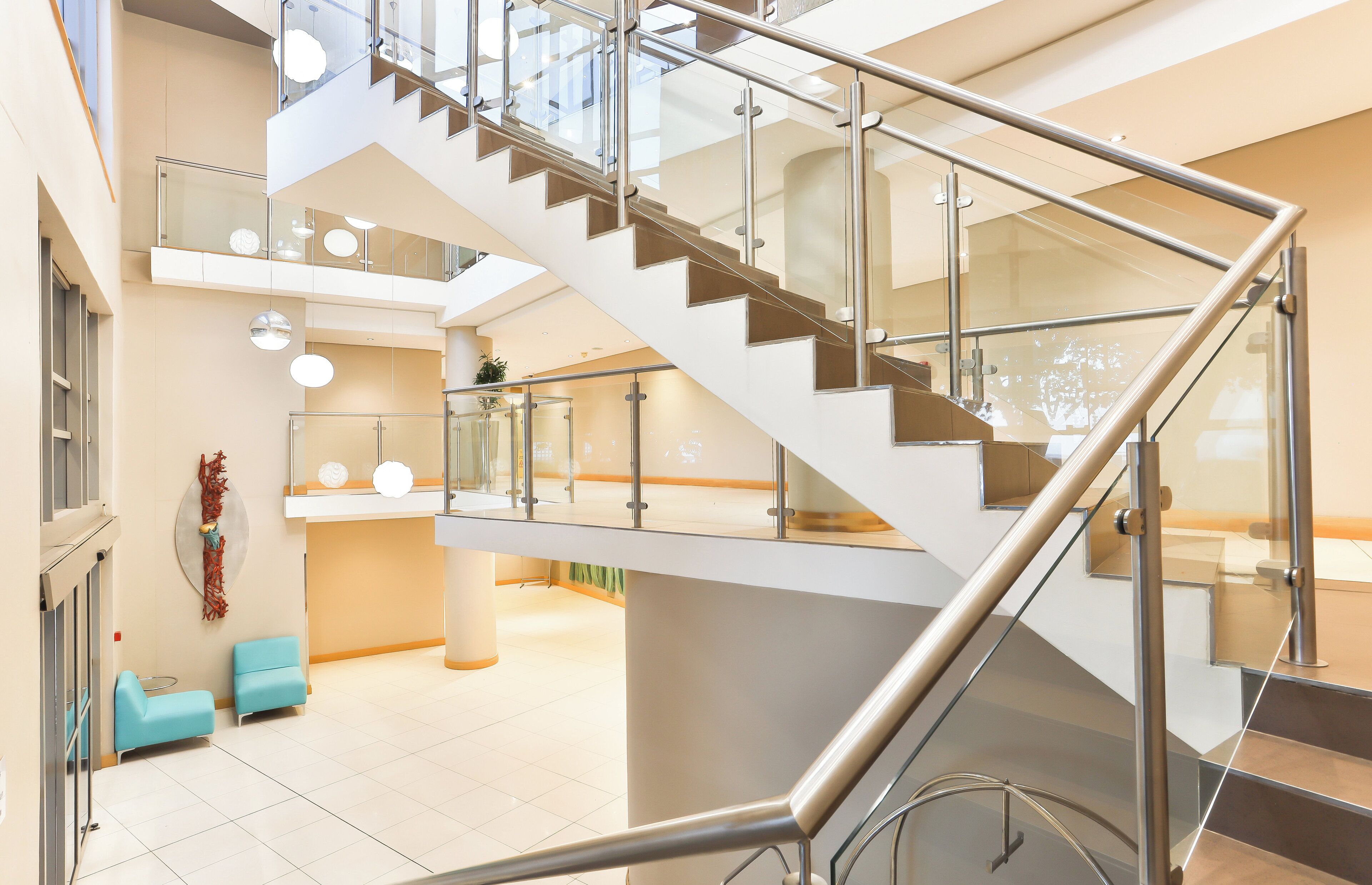 A modern interior with a glass and metal staircase, a seating area with blue chairs, and a clean, bright atmosphere.