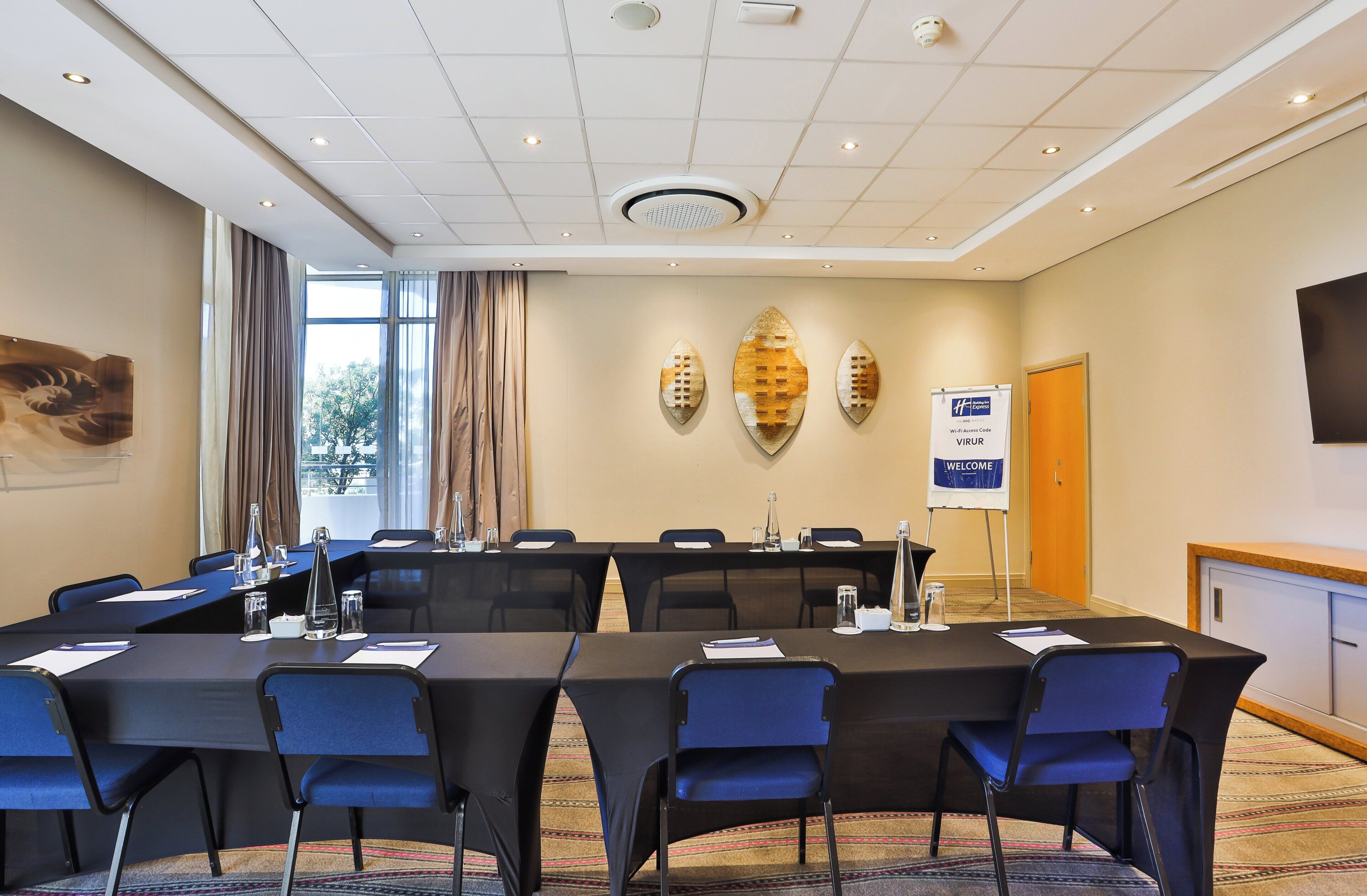Un salón de conferencias con una larga mesa, sillas, una pizarra y un letrero de bienvenida.