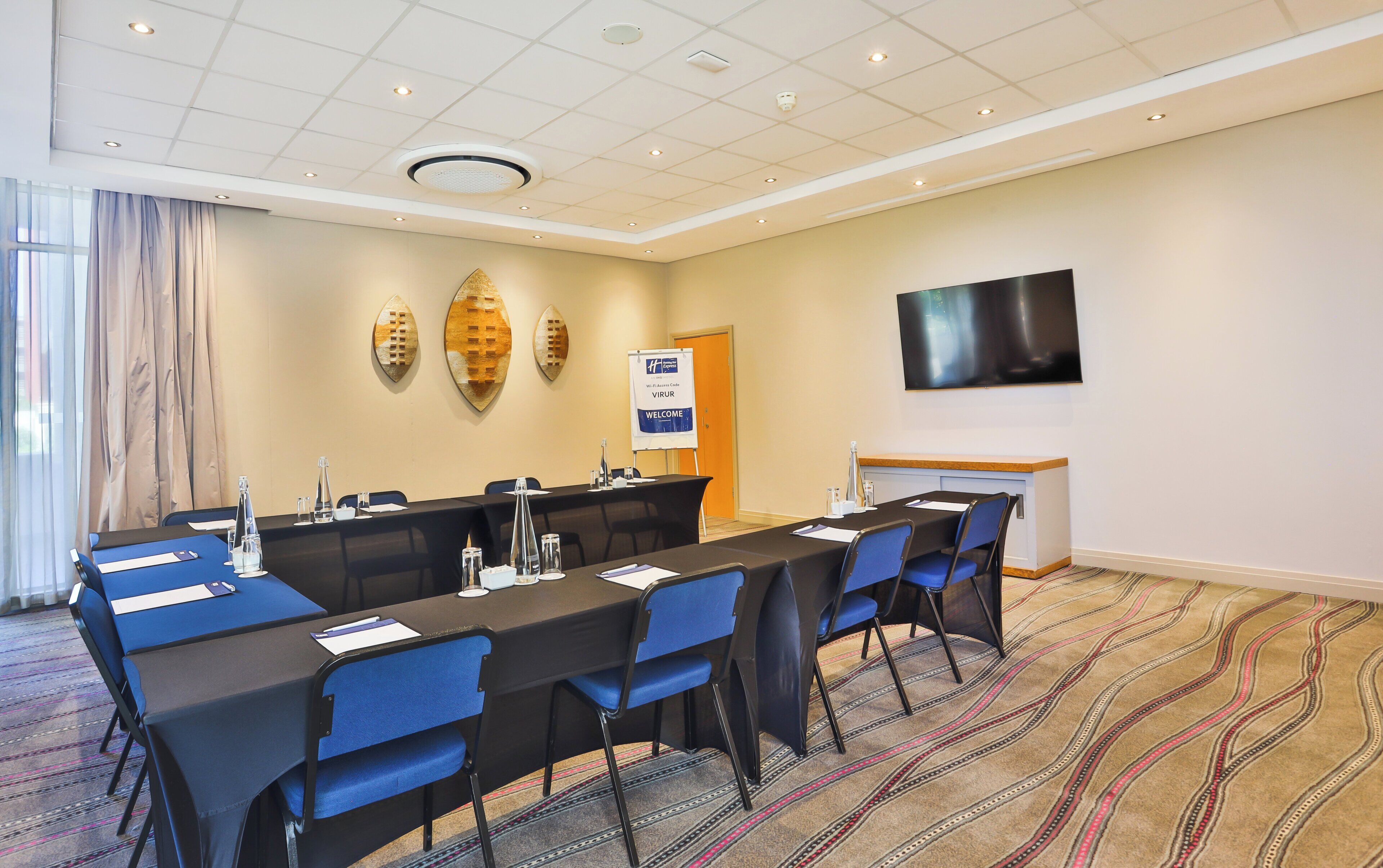 A conference room with a long table, blue chairs, a flat-screen TV, and a 'Welcome' sign.