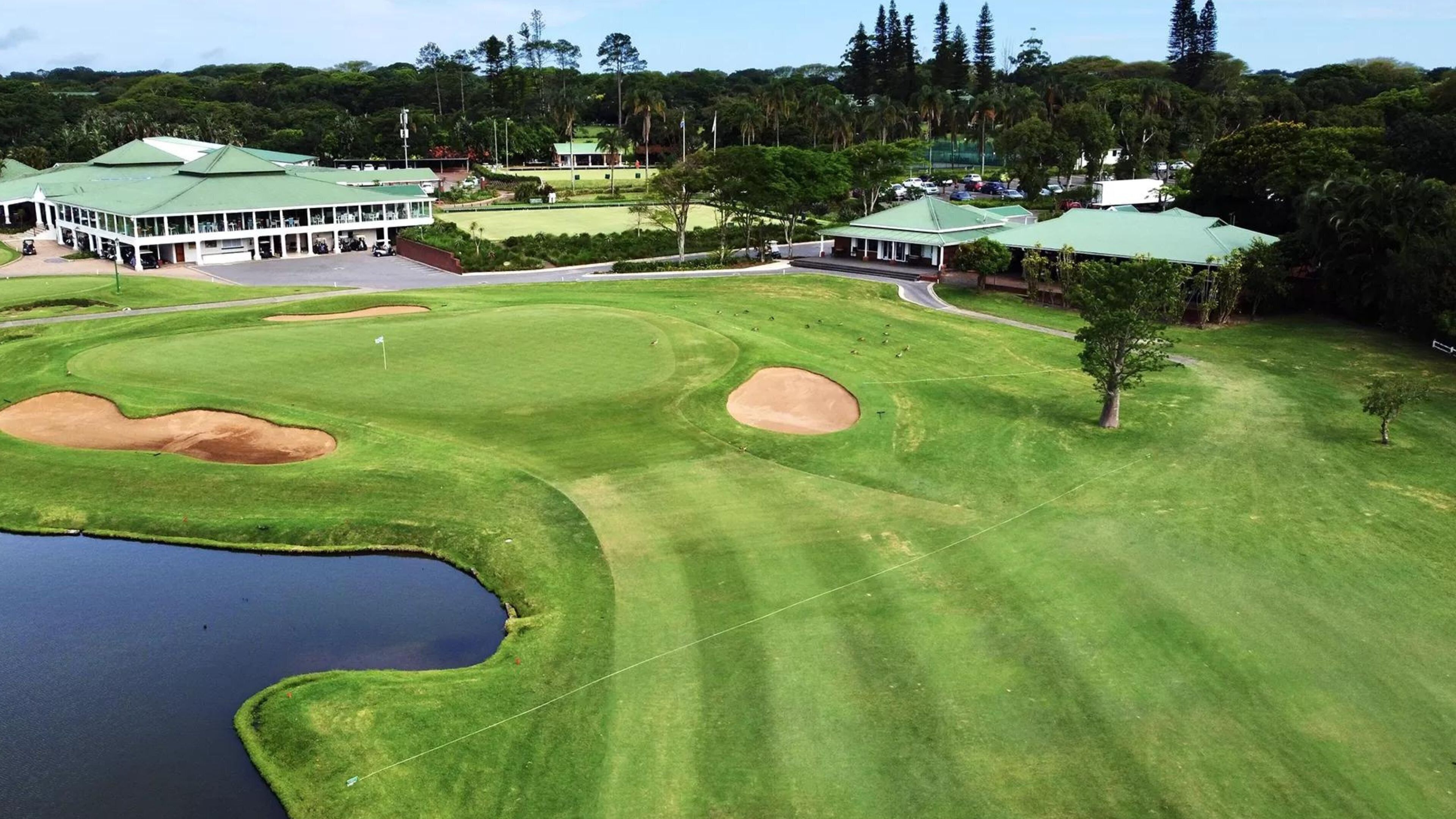 Un campo de golf con búnkeres, un estanque y edificios con techos verdes.