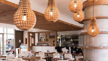 Interior de restaurante con vigas de madera en el techo, lámparas esféricas colgantes y una columna central. Las mesas están dispuestas con vasos y cubiertos.