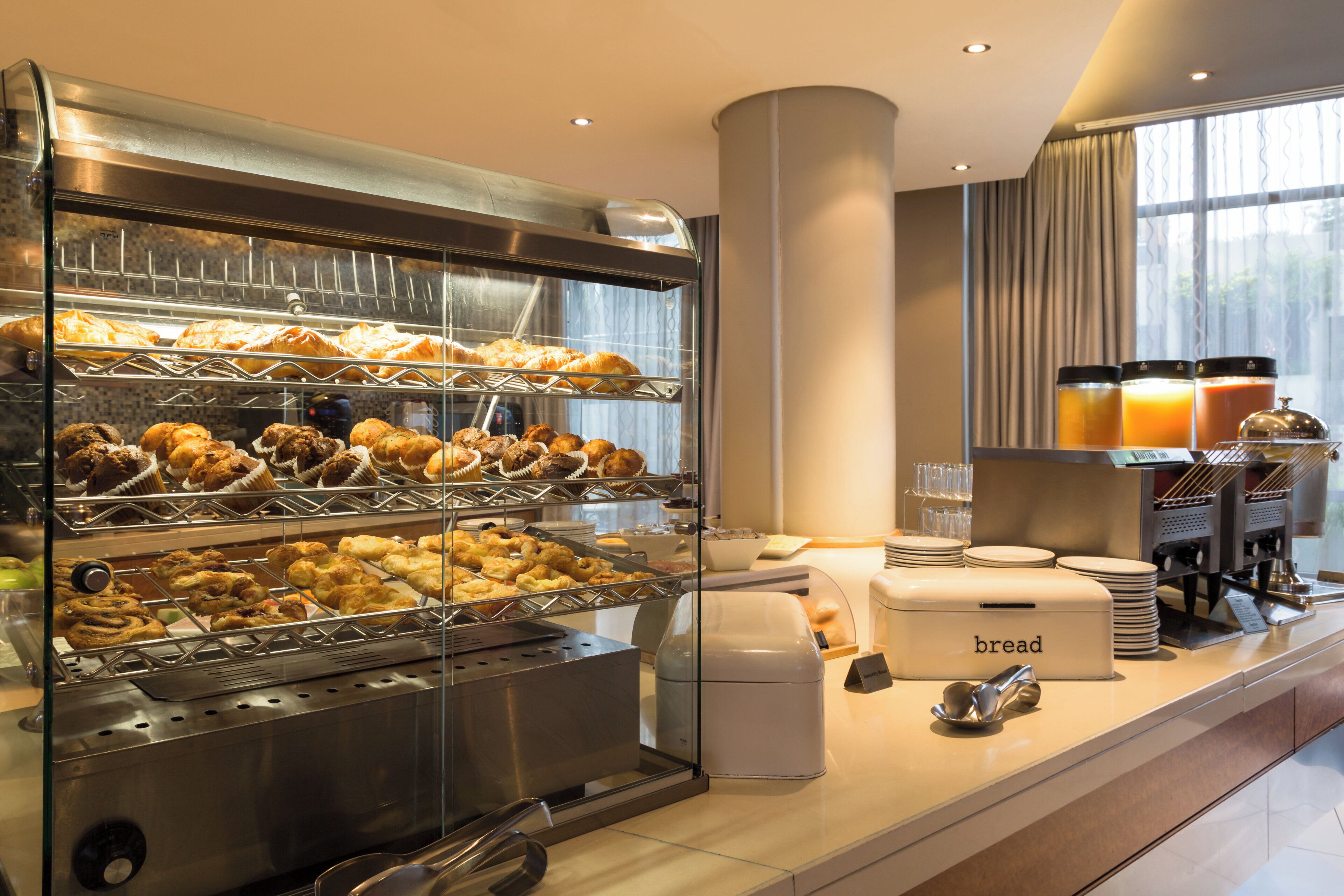 Un buffet de petit-déjeuner proposant diverses viennoiseries et pains, une machine à café et un distributeur de jus.