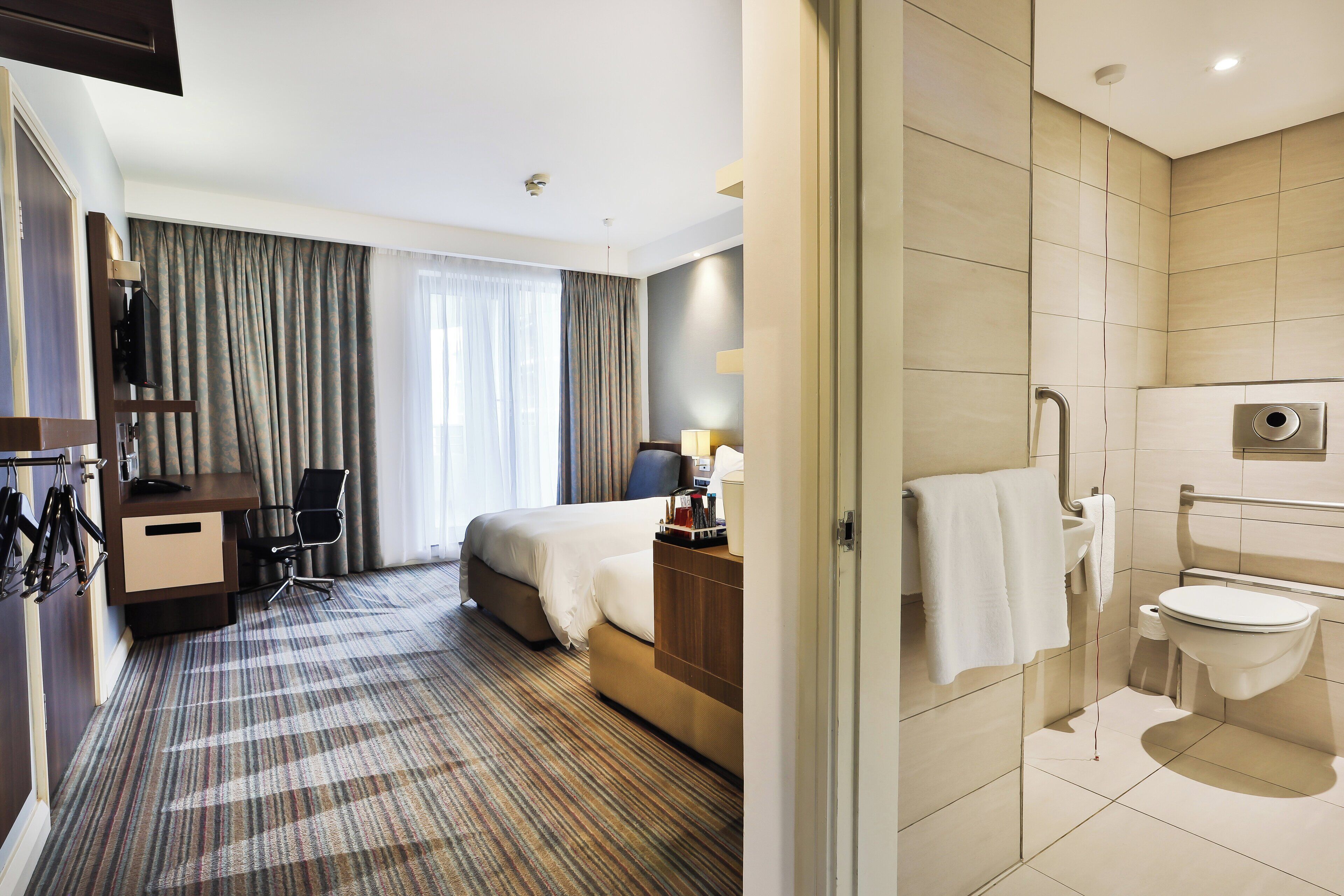 Una habitación de hotel con cama, escritorio, silla y baño con inodoro y lavamanos.