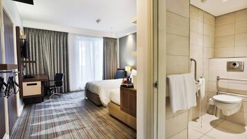 Una habitación de hotel con cama, escritorio, silla y baño con inodoro y lavamanos.
