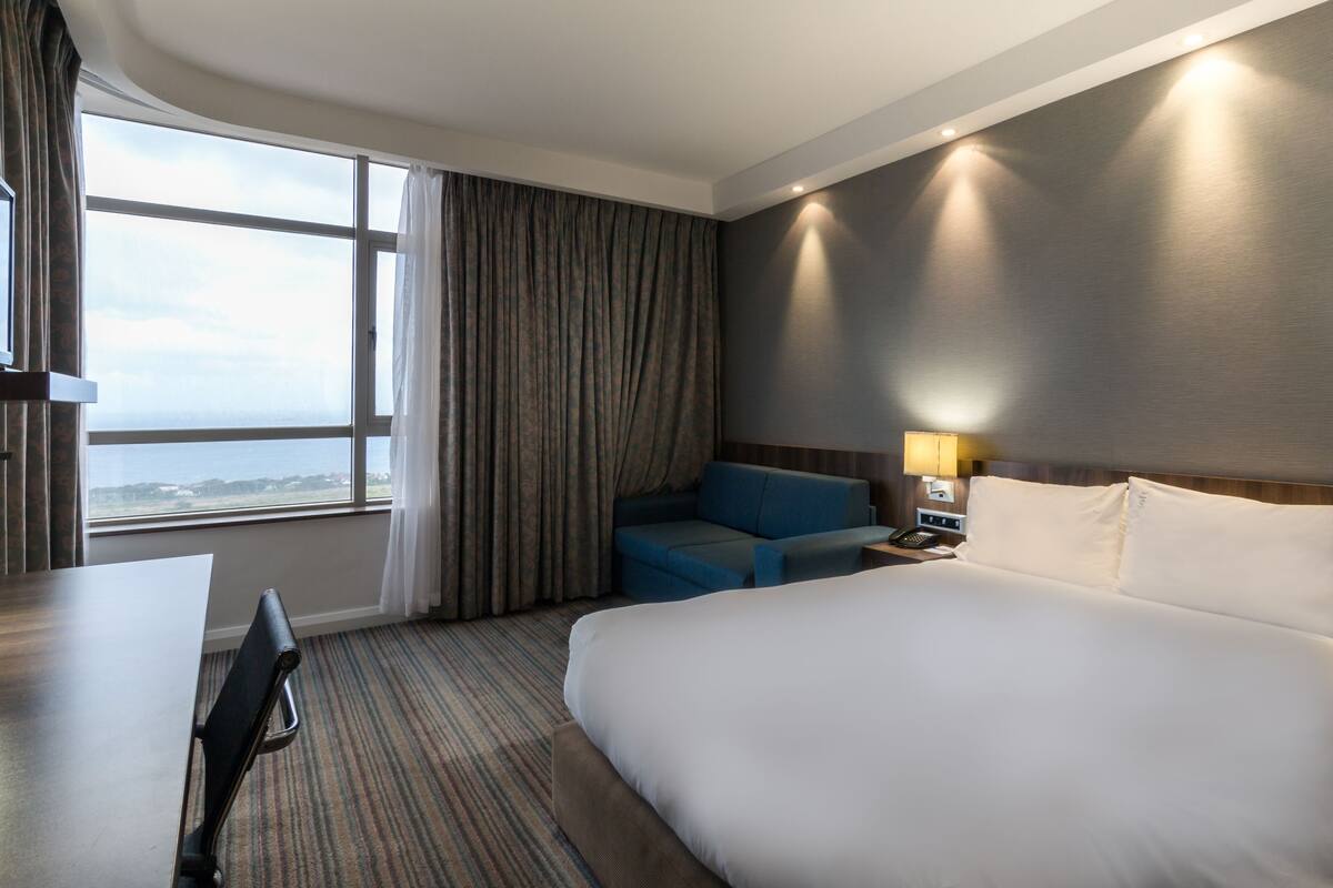 A hotel room with a large bed, a desk, and a view of the ocean through a window.