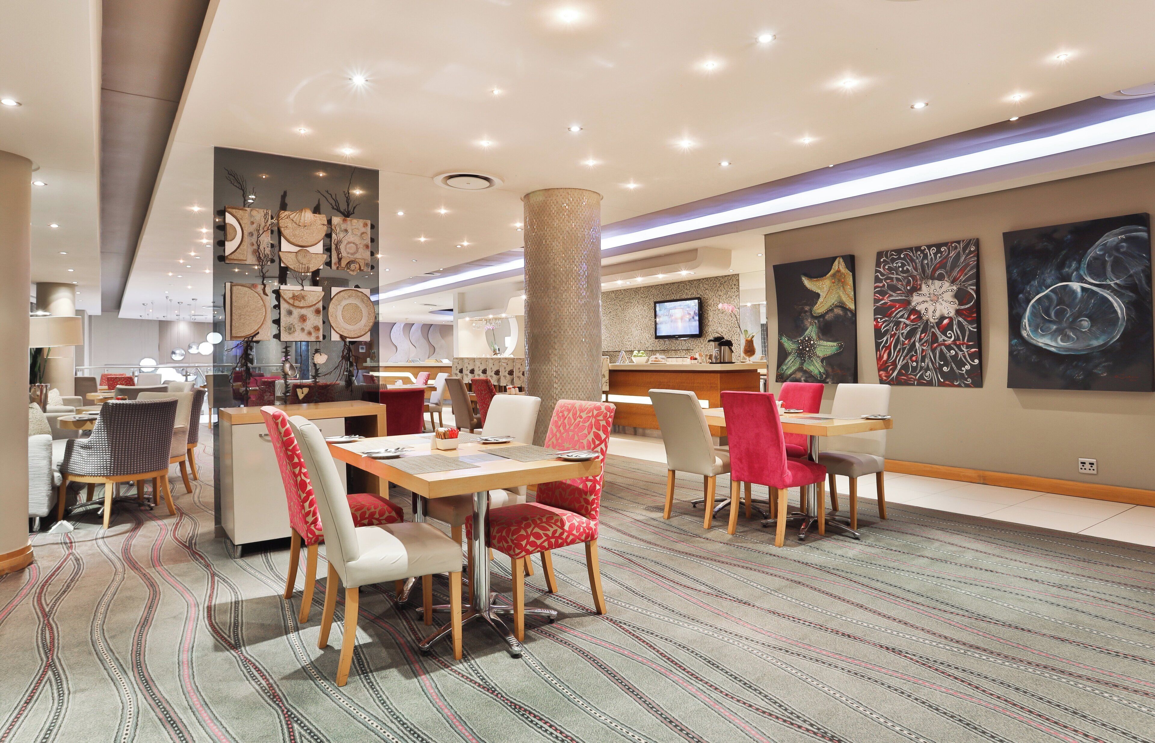A modern hotel lobby with a reception desk, seating area, and artwork on the walls.