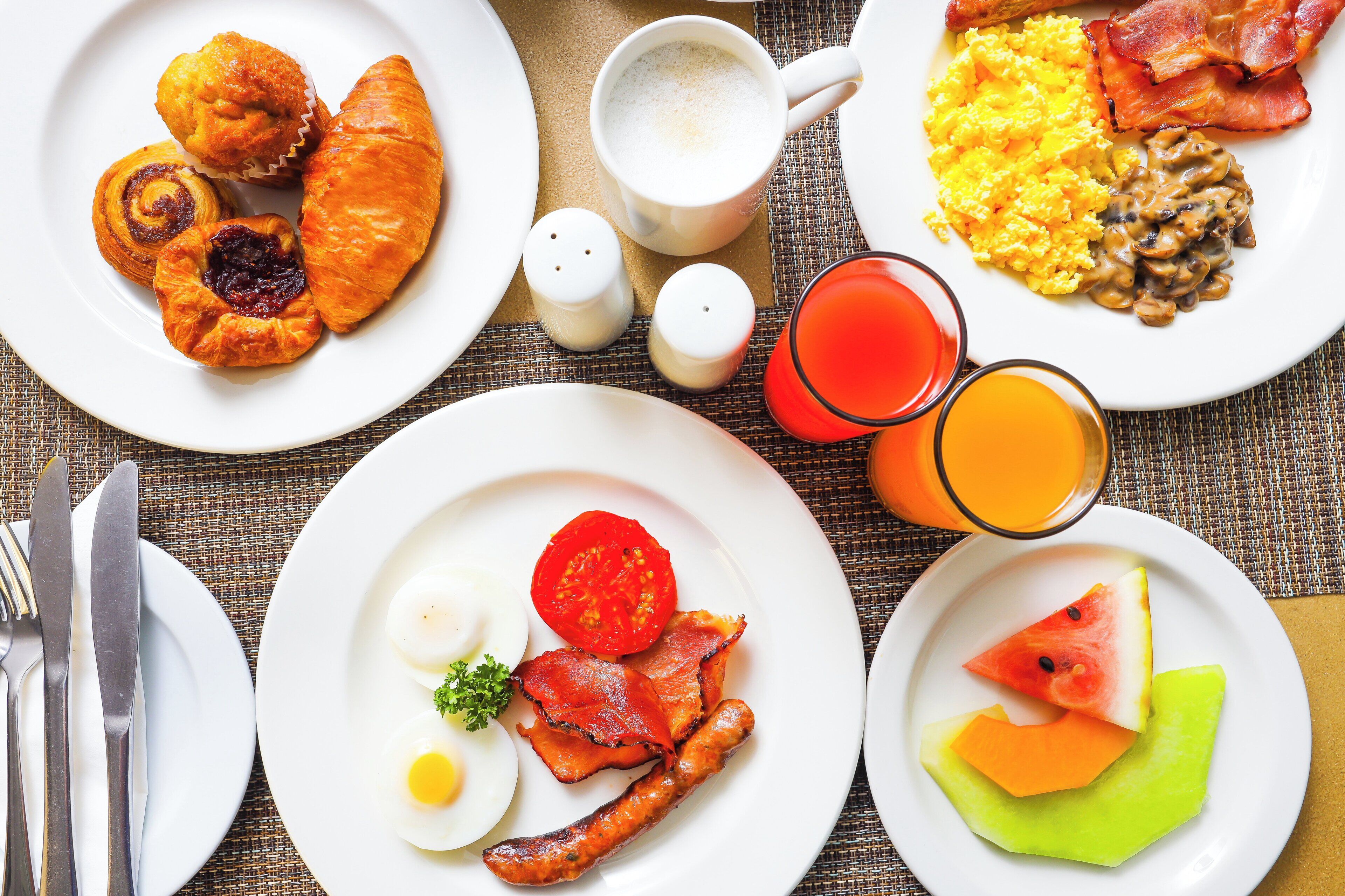 Une table dressée pour le petit-déjeuner, avec des assiettes contenant des œufs, du bacon, des toasts et des fruits.