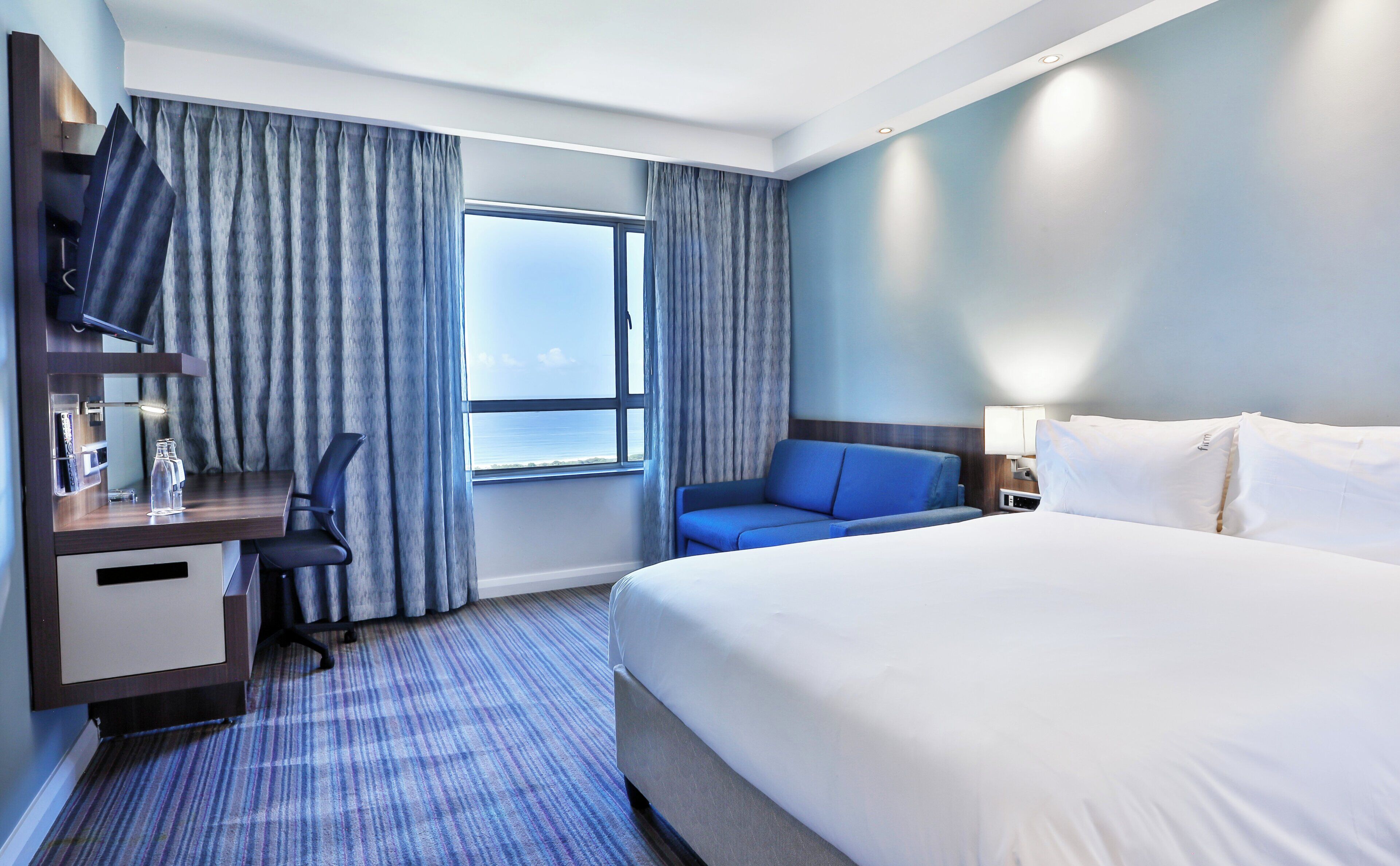Habitación de hotel con cama, escritorio con silla, televisión y ventana con cortinas.