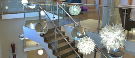 A modern interior with a glass staircase, metal railings, and contemporary lighting fixtures.