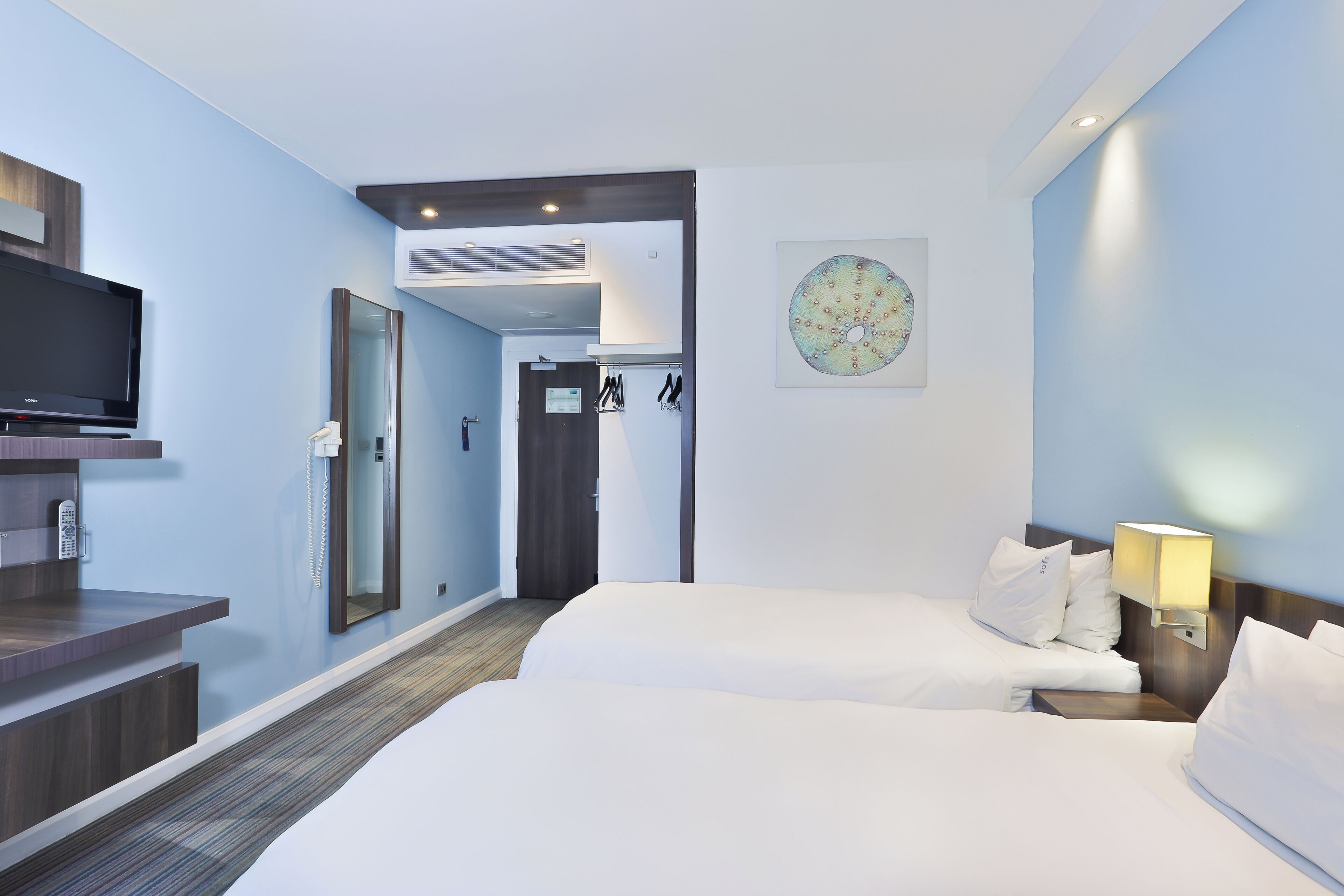A hotel room with two beds, a TV, a desk, and a bathroom door.