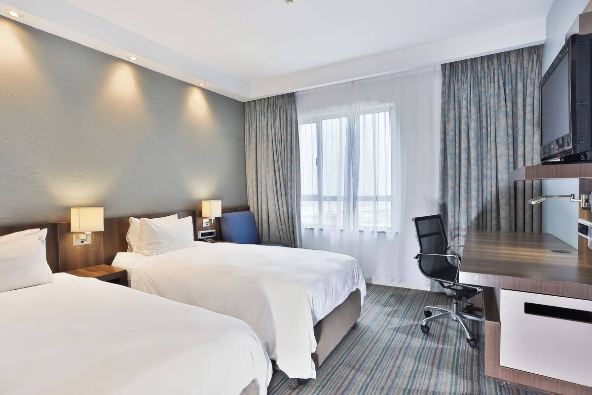 A hotel room with two beds, a desk, a chair, a television, and a window with curtains.