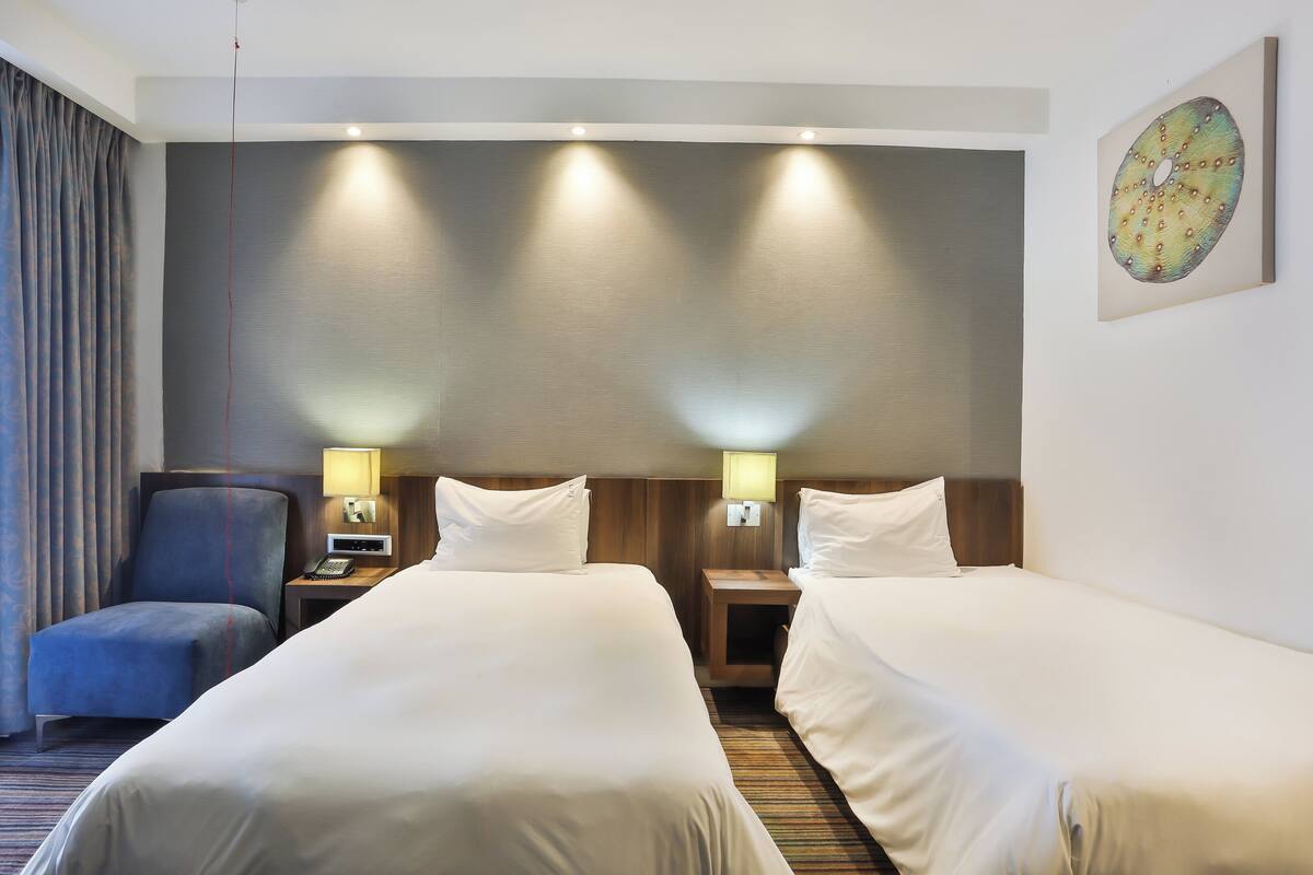 A hotel room with two beds, a desk, a chair, and a lamp.