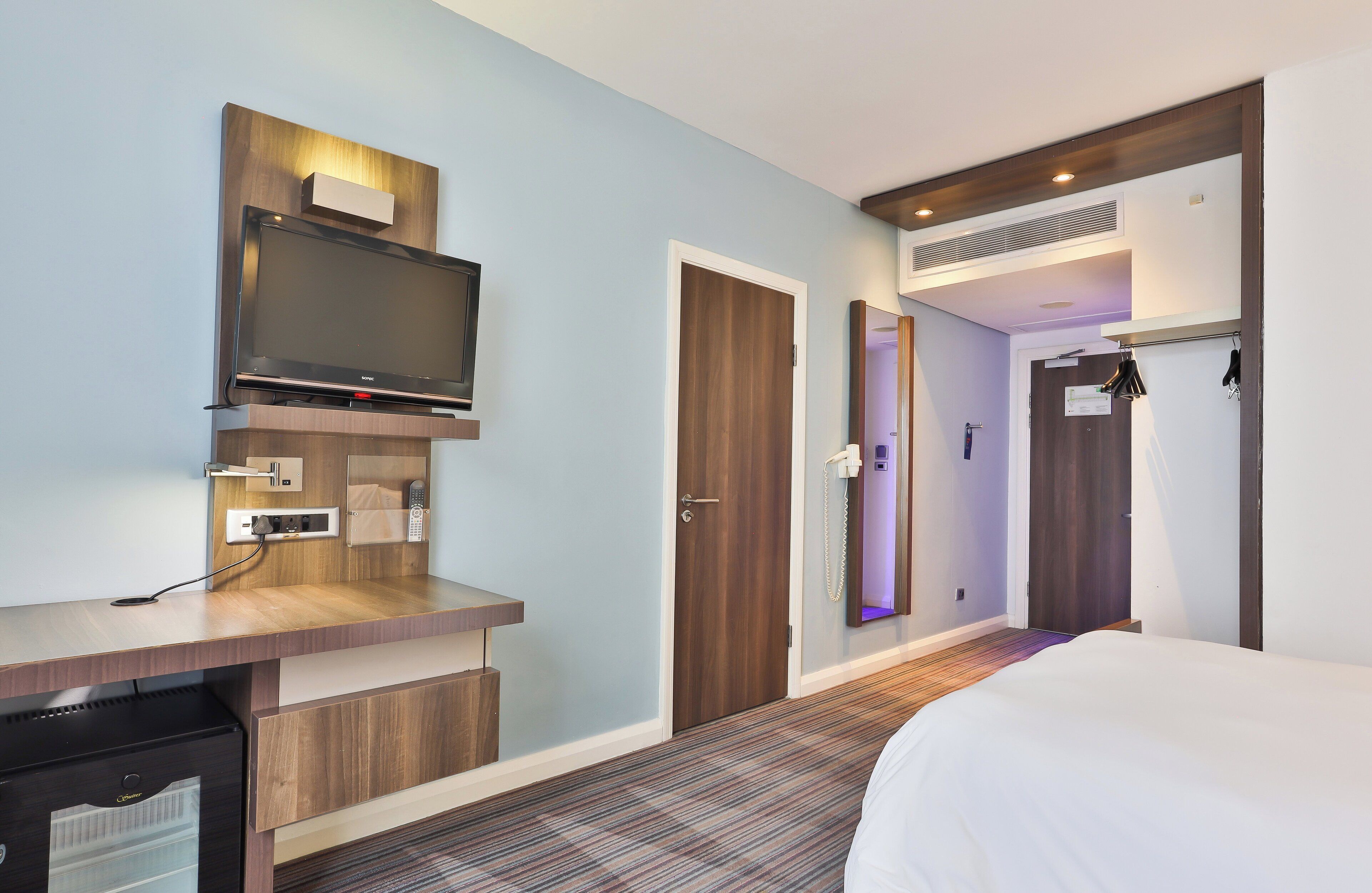 A hotel room with a flat-screen TV, a desk with a telephone, a wardrobe, and a bed.