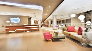Un hall d’hôtel moderne avec un comptoir d’accueil, un espace salon et une table basse en verre.