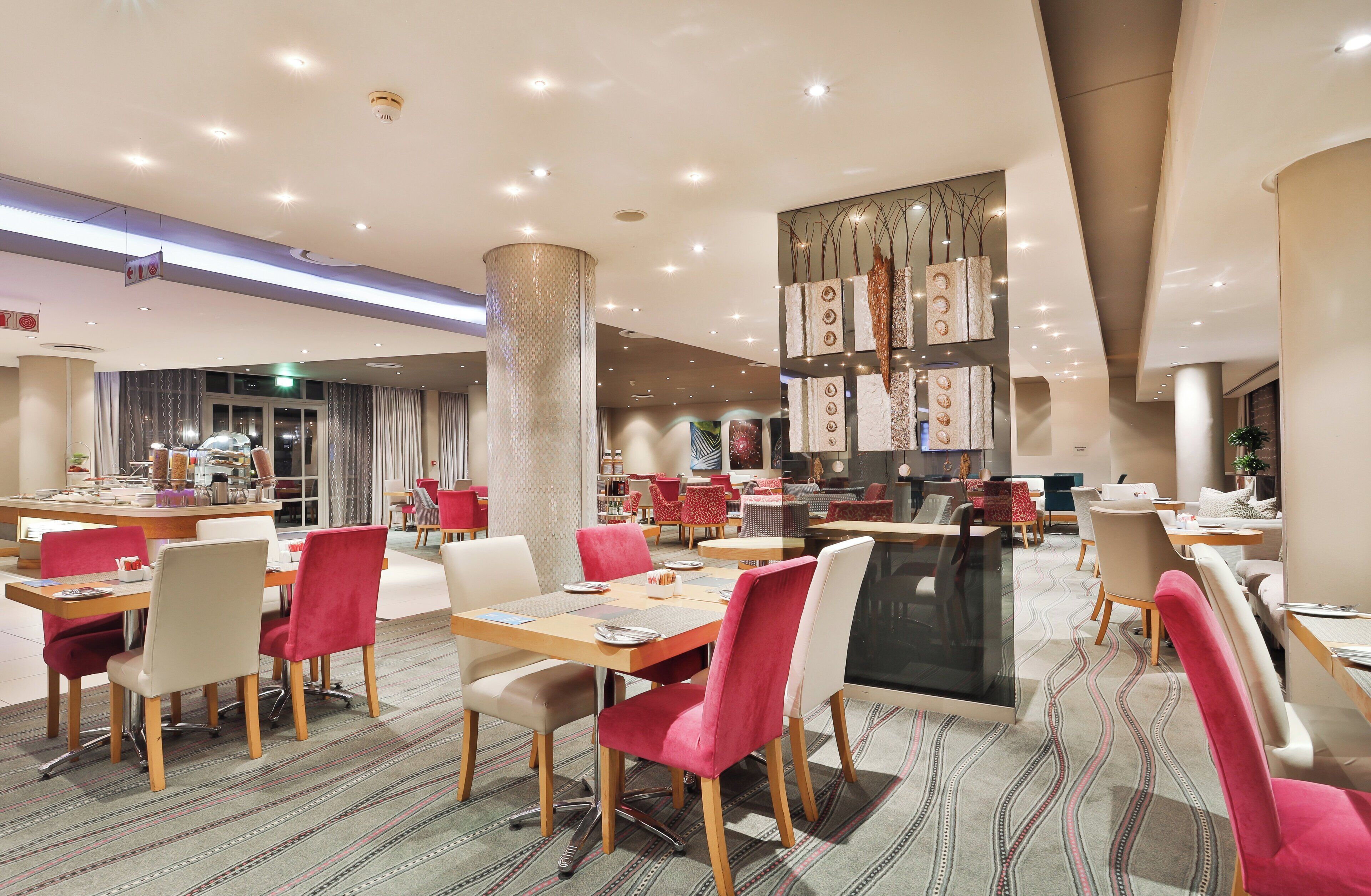 Un espace de restauration moderne, doté de plusieurs tables et chaises, d’un pilier central et d’un tapis à motifs.