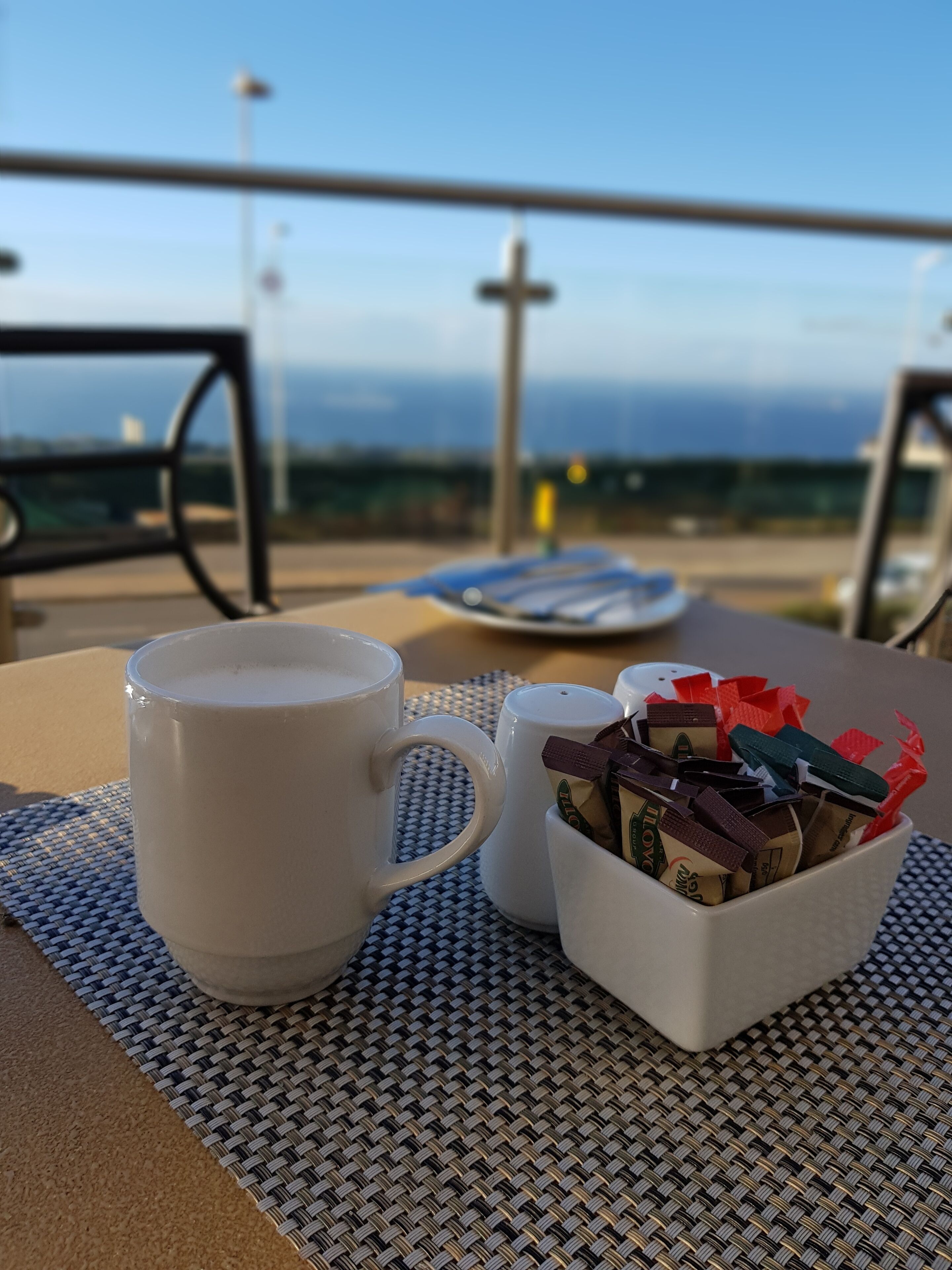 A table with a white mug and a salt shaker filled with chocolate bars, set on a woven mat.