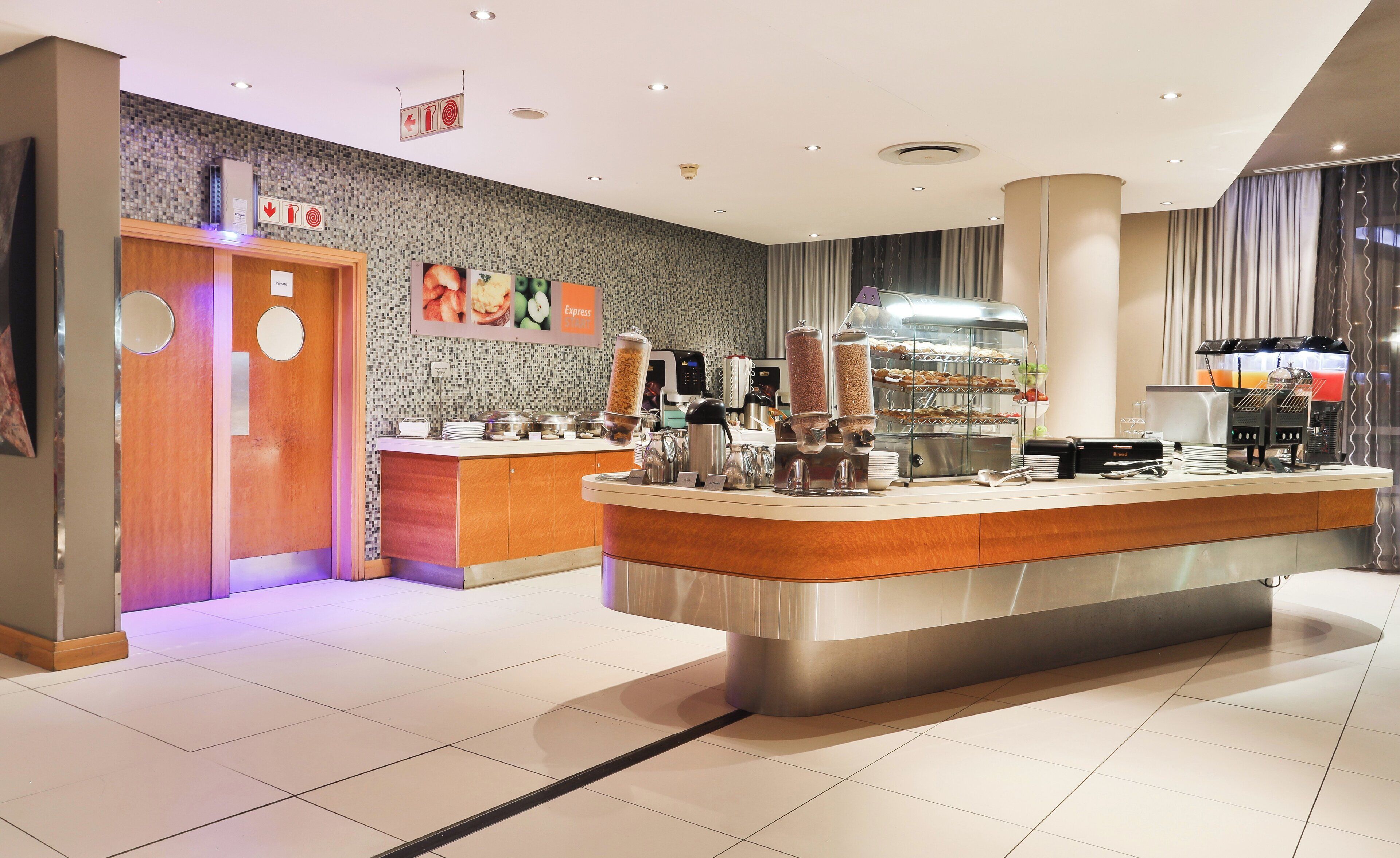 A modern hotel lobby with a central reception desk, a coffee machine, and a buffet area.