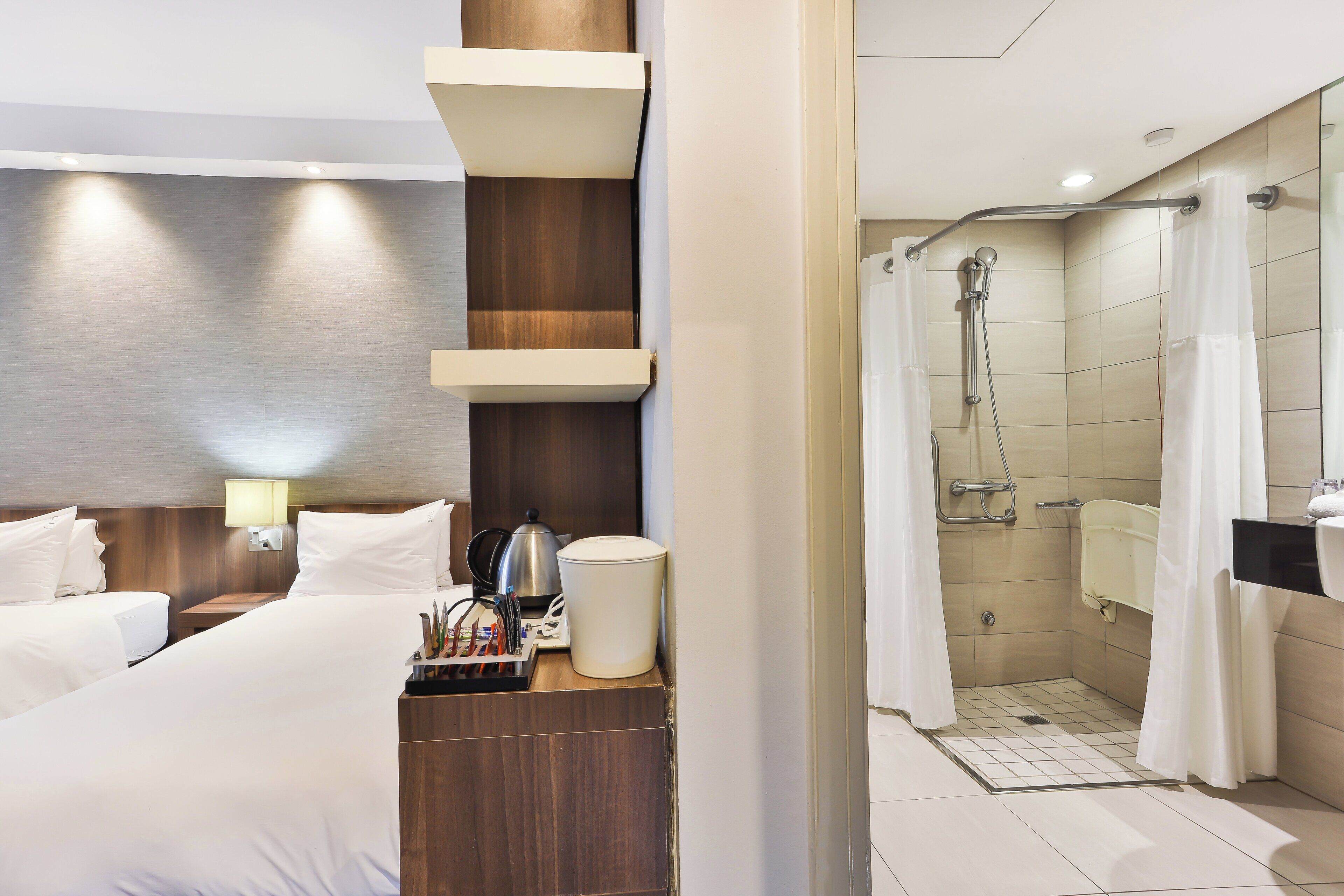 Une chambre d’hôtel comprenant un lit, une table de chevet, une lampe et un espace douche doté d  ’une porte en verre.