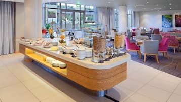 A modern breakfast buffet with a variety of food options, a seating area with colorful chairs, and a view of the outdoors through large windows.