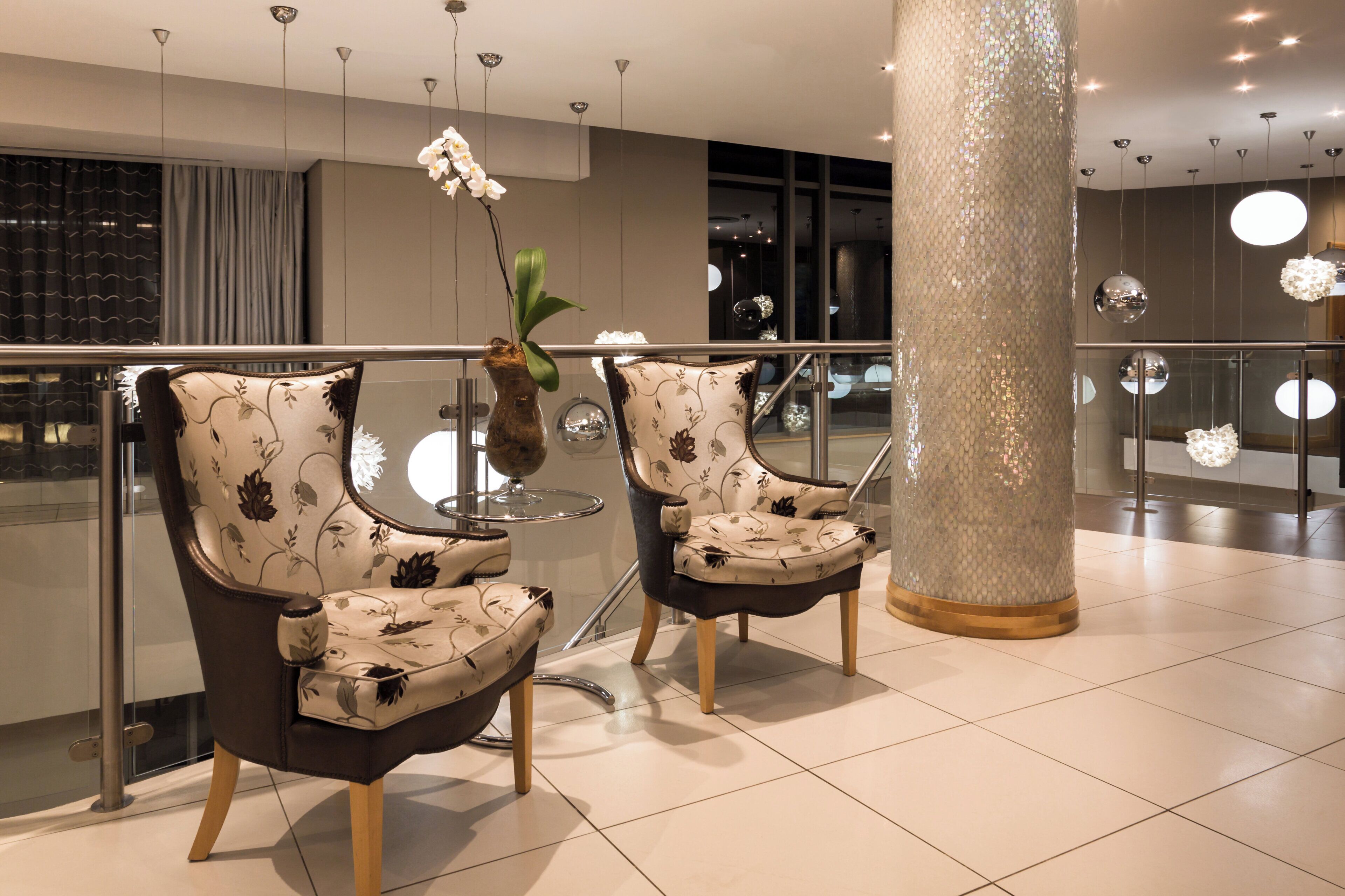 Two upholstered chairs with a floral pattern, a vase with a plant, and a decorative column in a modern interior space.