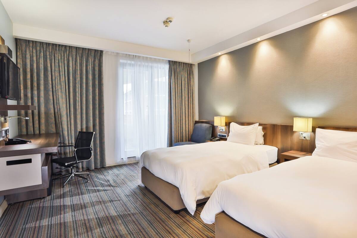 A hotel room with two beds, a desk, a chair, and a TV.