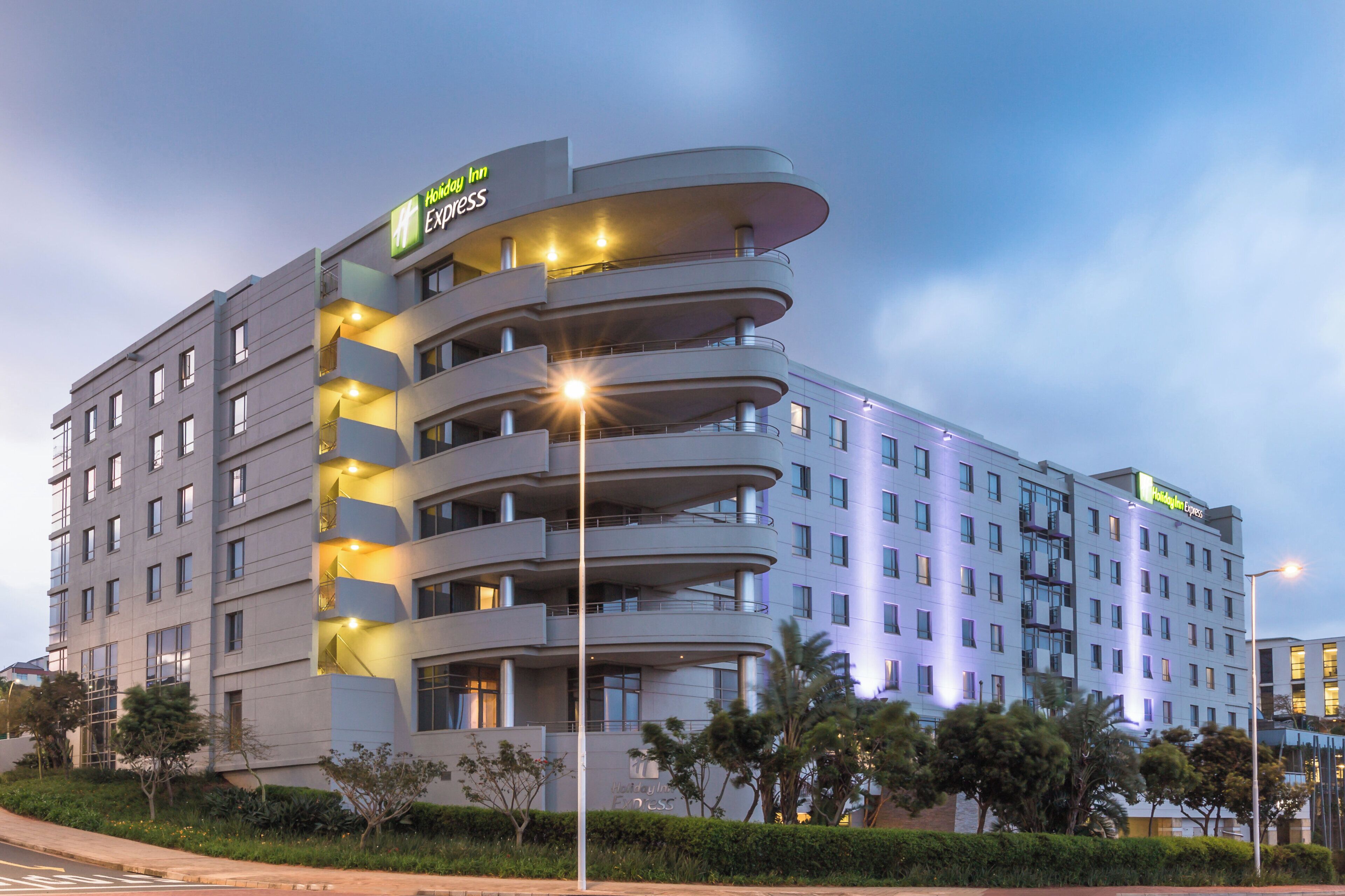 A multi-story Holiday Inn Express hotel with a modern design, featuring balconies on each floor and a well-lit facade.