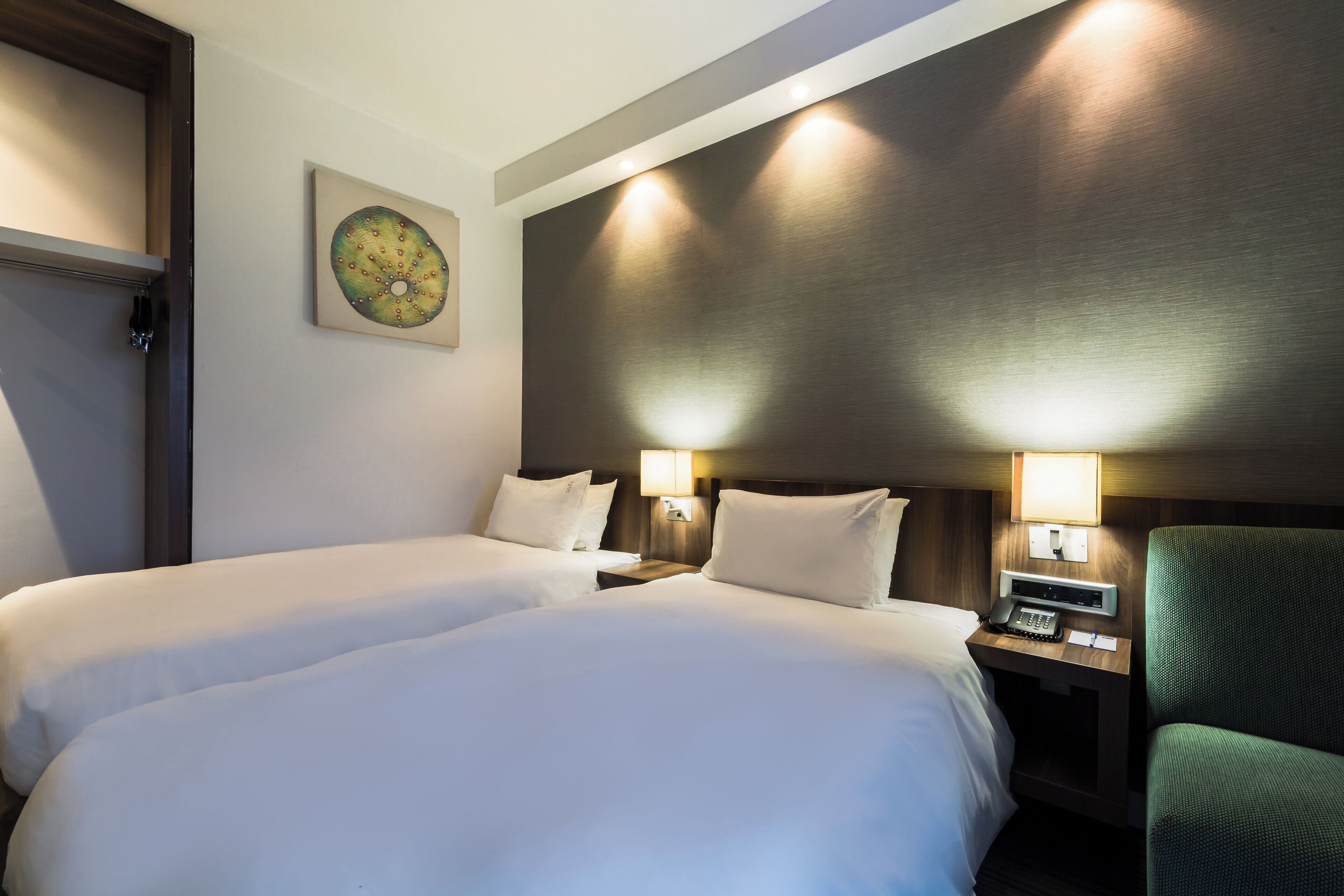 Une chambre d’hôtel avec deux lits, une table de chevet avec une lampe, un téléphone et une chaise.