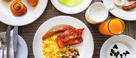 Uma mesa de café da manhã com ovos, bacon, cogumelos, croissants e frutas.