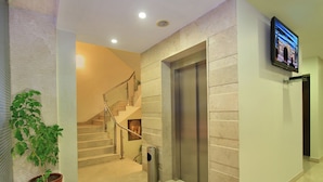 A modern hotel lobby with a marble staircase, a trash bin, a potted plant, and a television mounted on the wall. - La Sara Hometel (Bengaluru)
