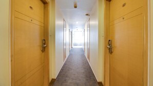 A long, narrow hotel corridor with wooden doors on both sides and a carpeted floor. - La Sara Hometel (Bengaluru)