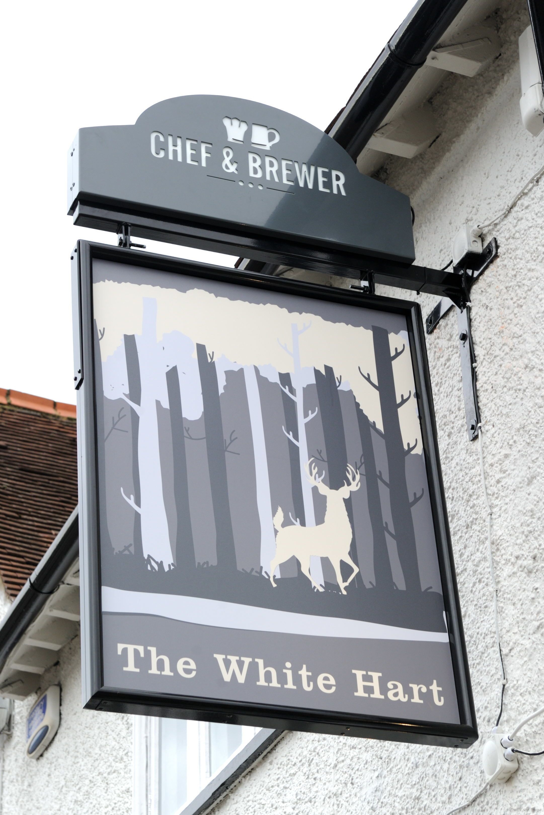 A sign for "The White Hart" pub with a forest silhouette and a chef's hat.
