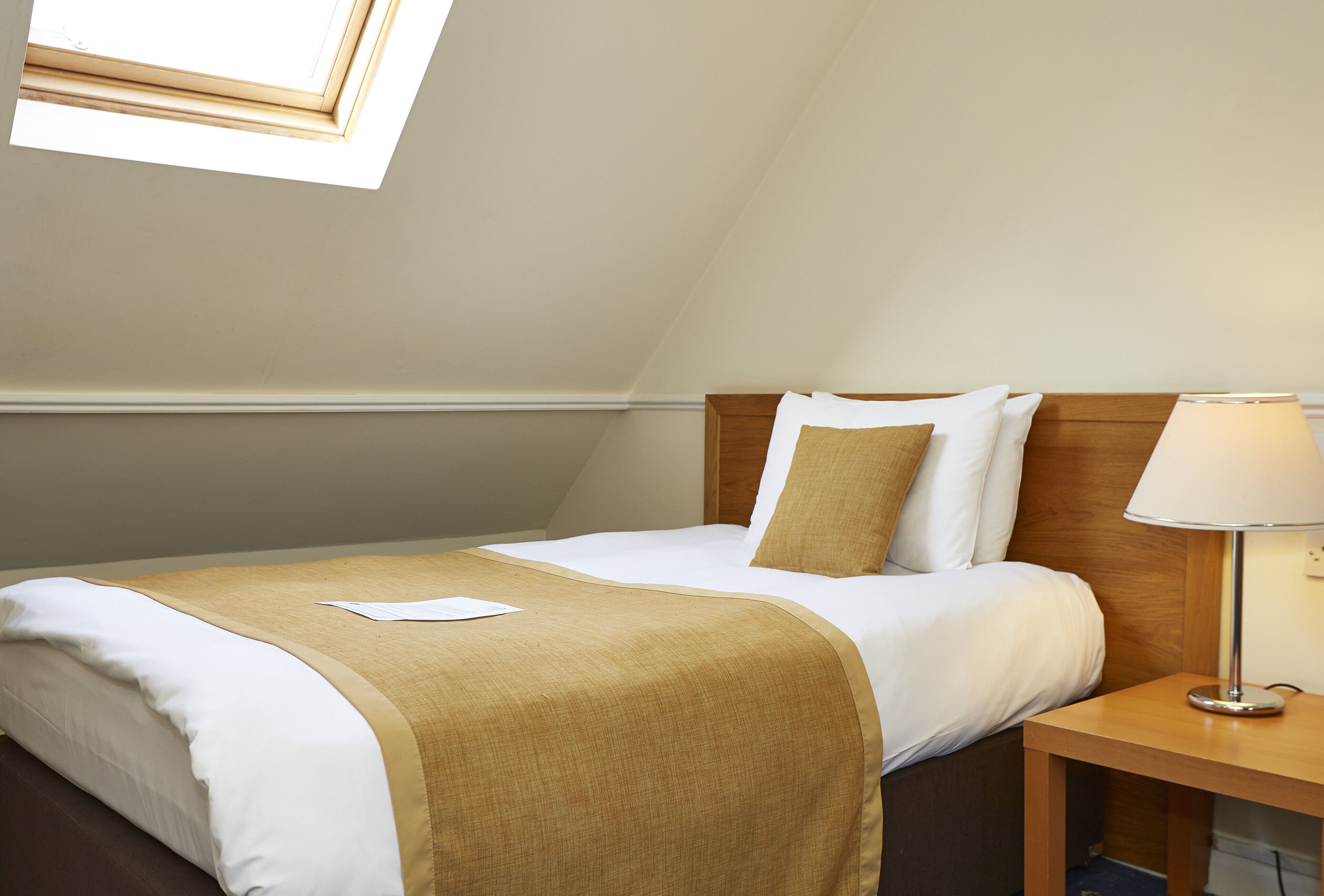 A neatly made bed with a beige and white bedspread, a wooden headboard, and a bedside lamp.