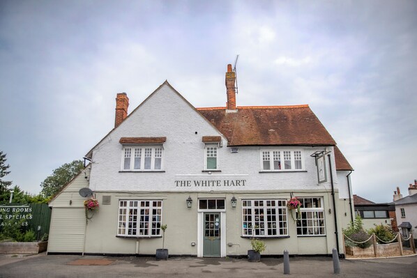 En toetages bygning, der hedder "The White Hart", i traditionel arkitekturstil, med en grøn dør, flere vinduer og en murstens skorsten.